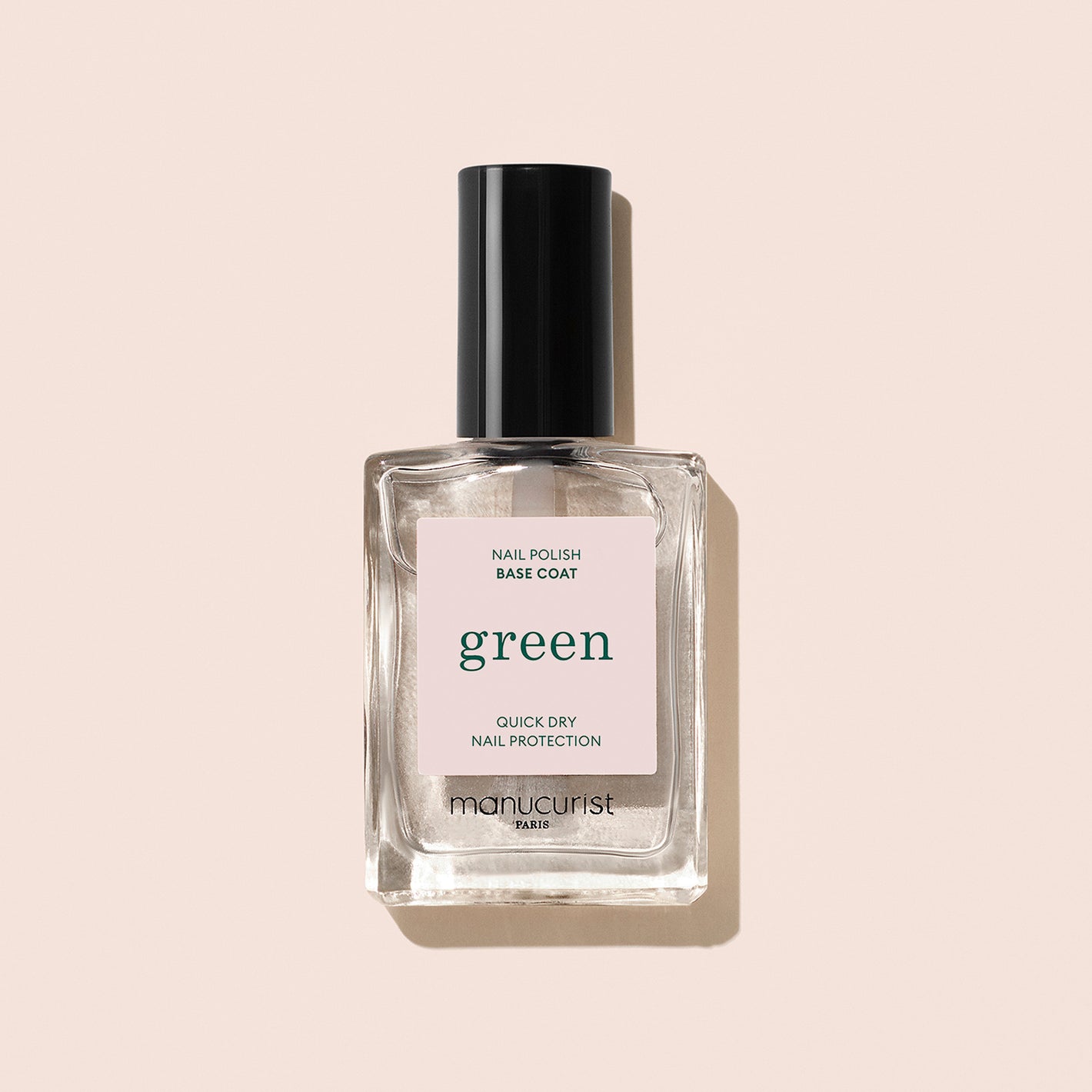 A clear glass bottle of Manucurist Base Coat nail polish with a black cap sits on a light beige background. The label reads "Base Coat," highlighting nail protection and quick-dry benefits for better polish adherence.