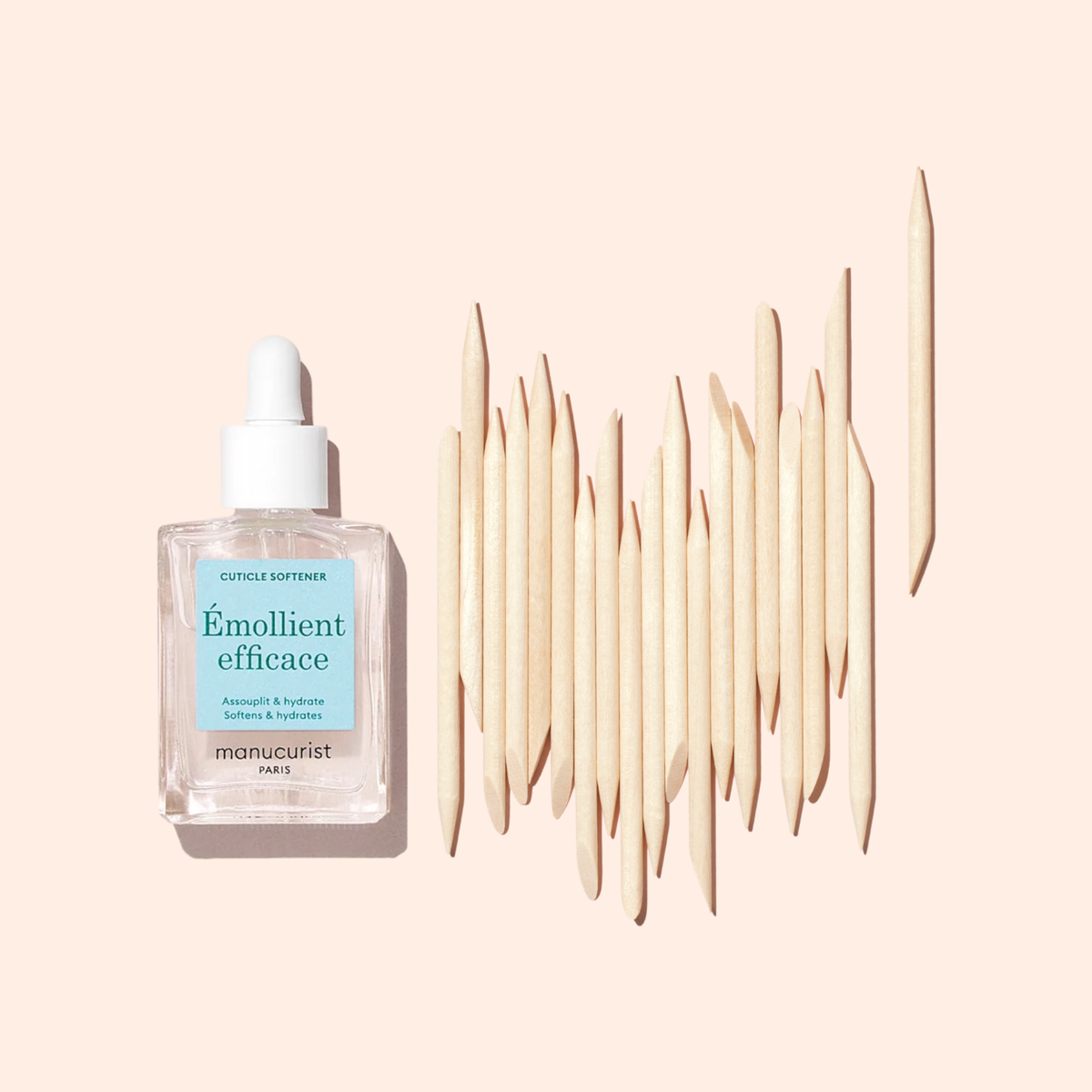 A bottle of cuticle softener with a dropper is displayed beside Manucurist-test Wooden cuticle stick x20, all neatly arranged on a light beige background.