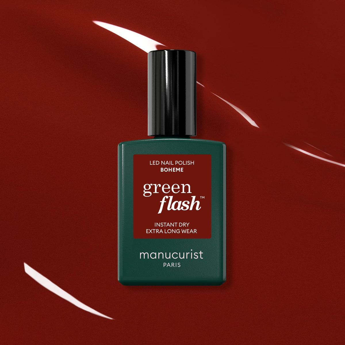 A bottle of Manucurist Bohème, a chic red-brown polish, stands centered on a glossy, deep red background with reflective highlights.