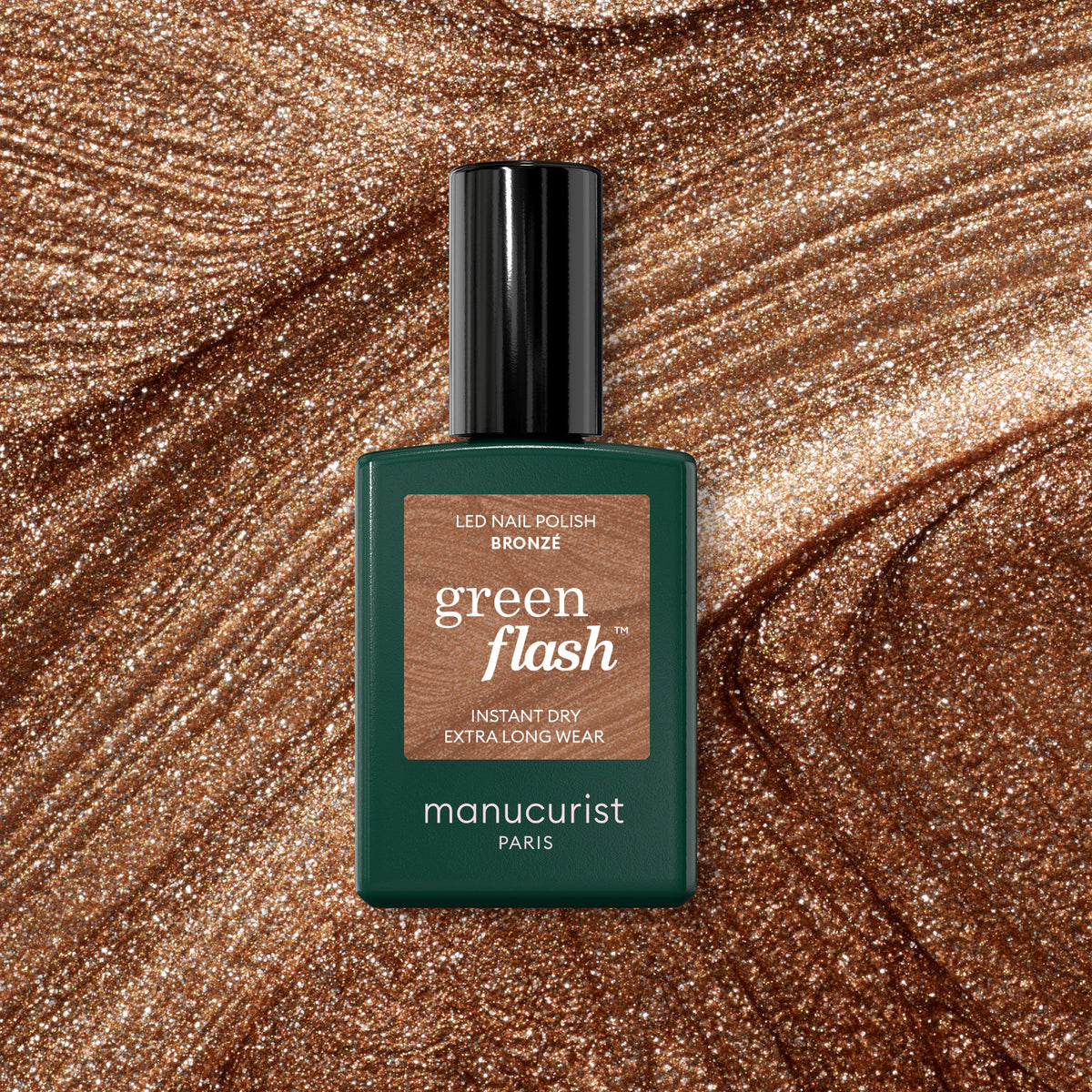 A bottle of Bronzé by Manucurist sits on a bronze glitter background, reflecting the nail polish’s coppery shine.