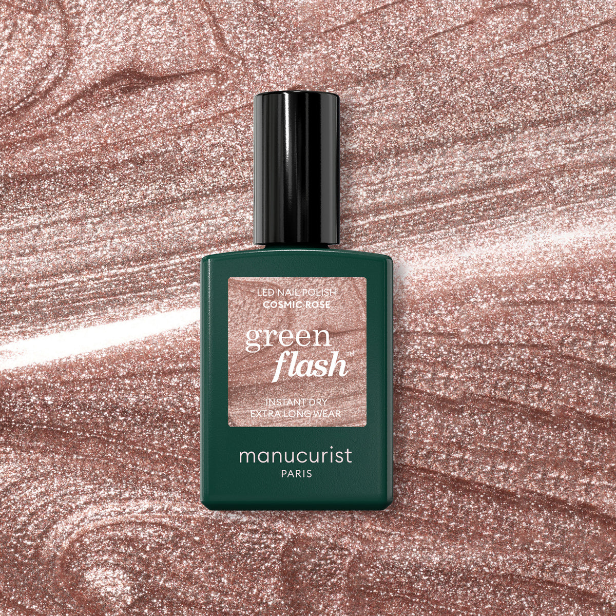 A bottle of Manucurist Cosmic Rose gel polish sits on a shimmery, rose-hued background that matches its iridescent pink shade. The green bottle with a black cap highlights the polish perfectly.
