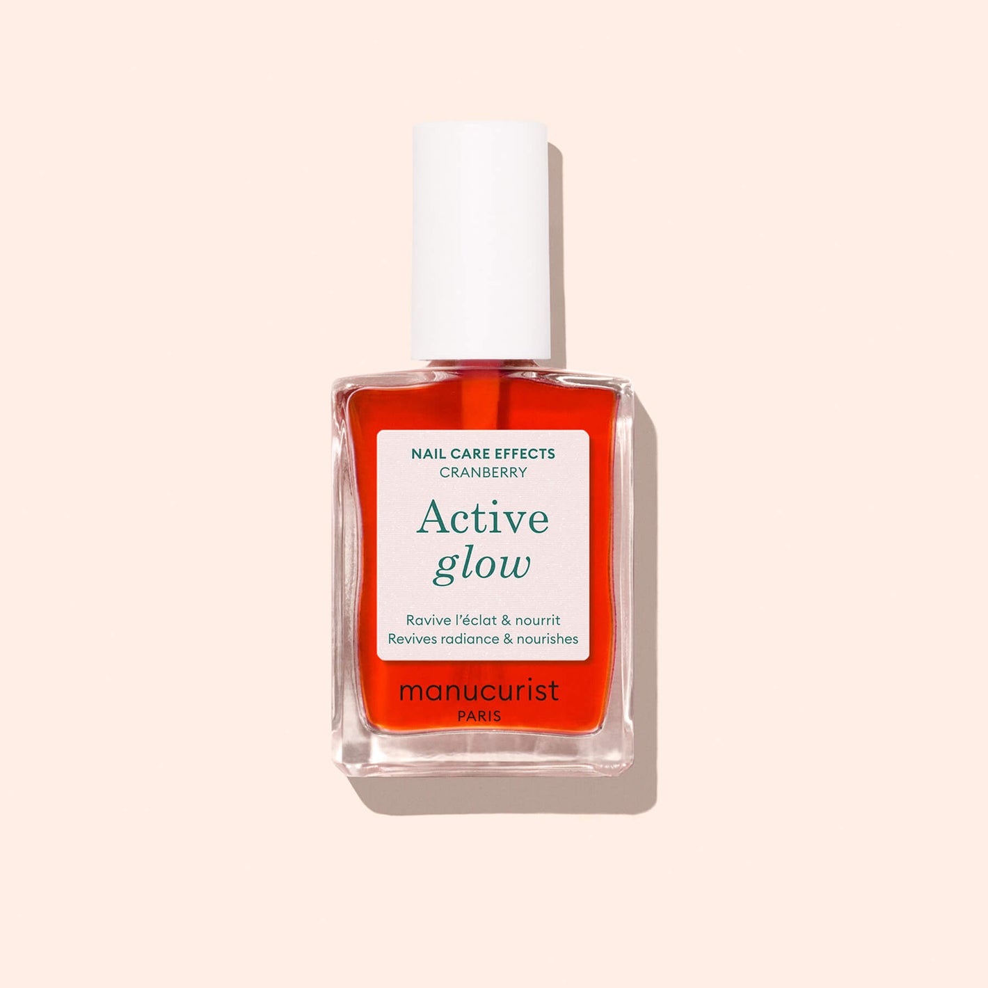 A bottle of Manucurist Active Glow Cranberry nail care treatment, with a plant-based formula, white cap, and clear label, is shown on a light beige background.