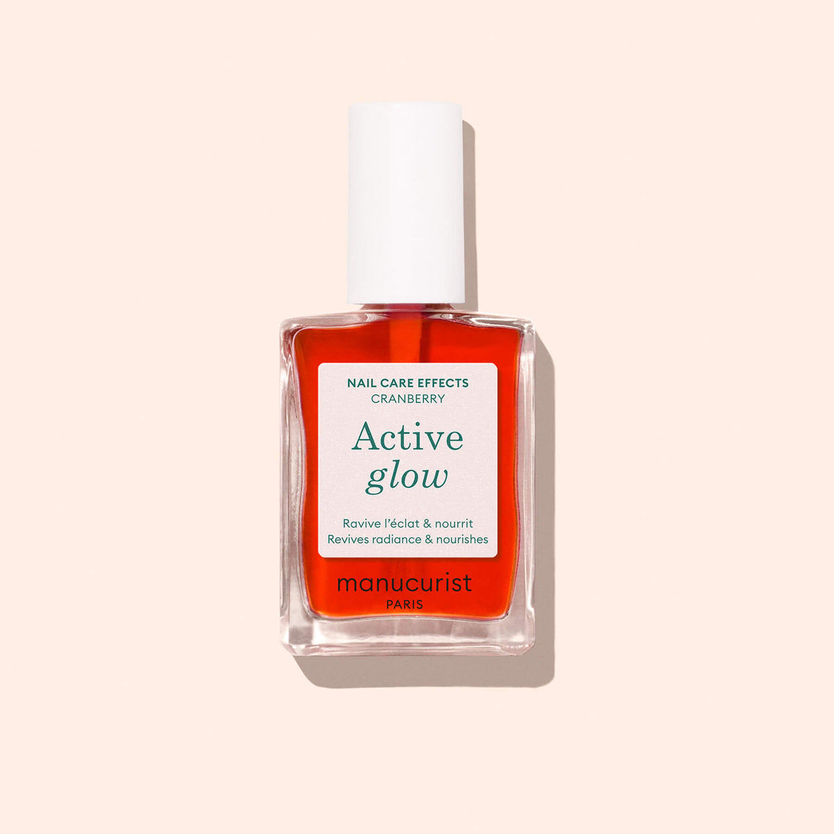 A clear bottle of Manucurist Active™ Glow Cranberry nail treatment, featuring a plant-based formula and a white cap, is set against a light beige background.