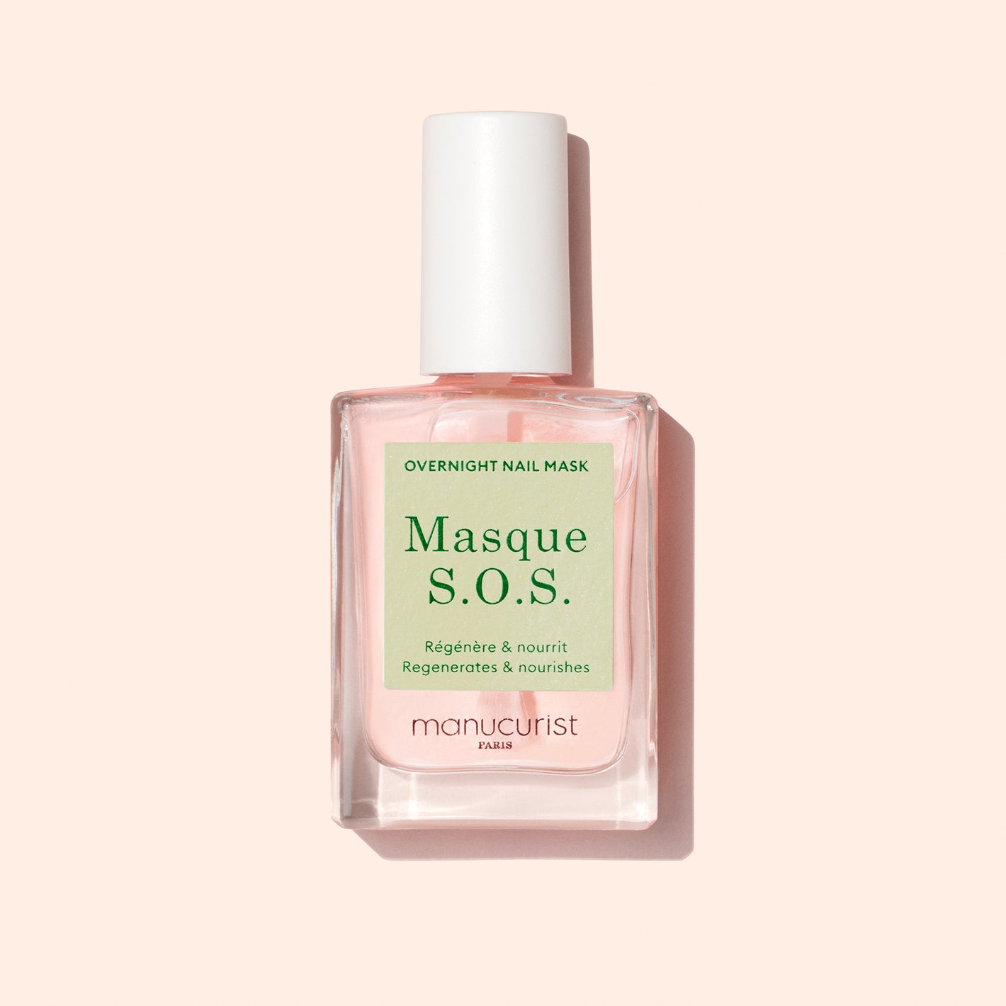 A bottle of Manucurist S.O.S. Nail Mask with a white cap and pale pink liquid sits on a light pink background. The label has green and white text. This overnight mask is perfect for nail regeneration.