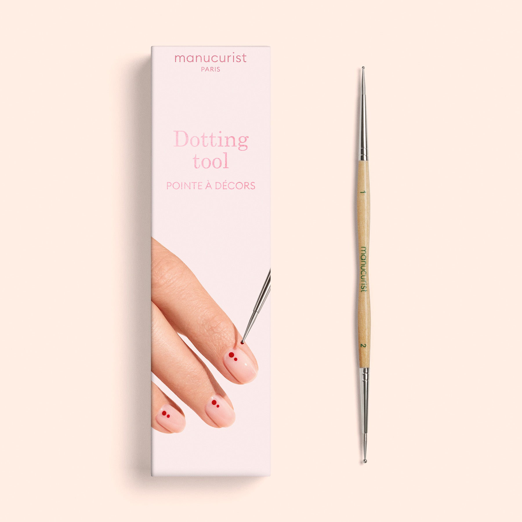 A professional quality Dotting Tool by Manucurist, featuring a wooden handle, is displayed beside its pink box, which shows a hand using the tool to create red dots for stunning nail art on fingernails.