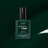A dark green bottle of Manucurist Green Flash LED gel nail polish in the shade Emerald is displayed against a matching green background, with a white reflection highlighting its deep, gemstone-inspired color.