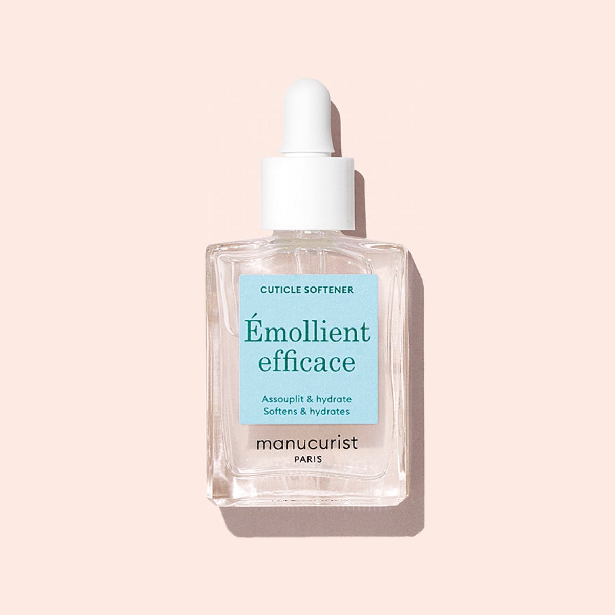 A clear glass dropper bottle of Manucurist Hydrating Cuticle Remover with a white cap and blue label, set against a light pink background—a must-have for any manicure routine.