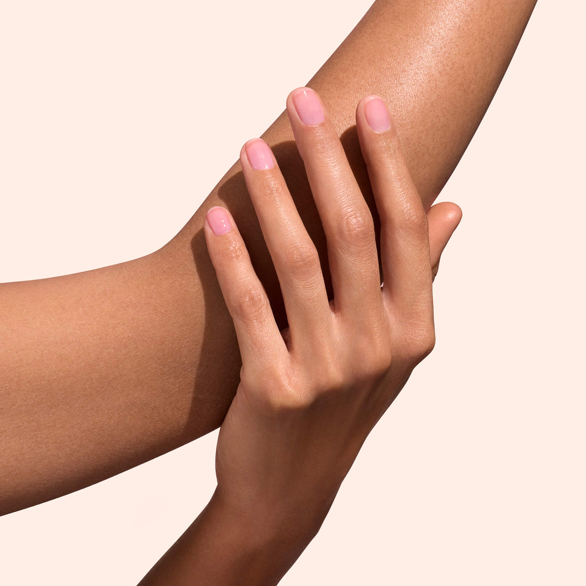 A close-up of a hand with neatly manicured, natural-looking nails featuring a subtle shine from Manucurist’s Active™ Glow Grape gently resting on a forearm against a light beige background.