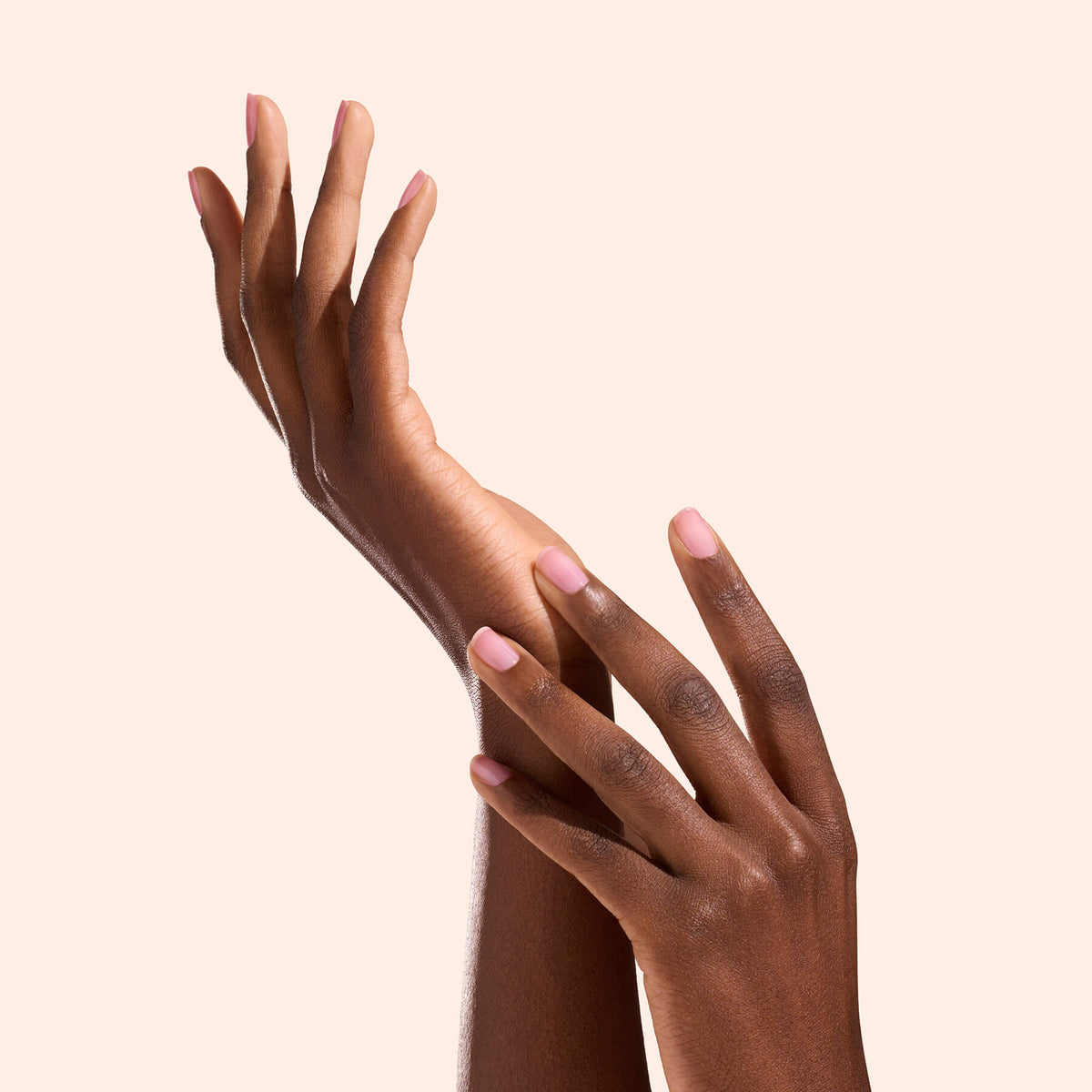 Two hands with neatly manicured nails, accentuated by the natural radiance of Manucurist’s Active™ Glow Grape treatment, are gracefully posed against a light beige background. The deep brown skin tone and elegantly extended fingers evoke a sense of softness and attentive care, while the healthy shine of the nails highlights the nourishing benefits of Active™ Glow Grape.