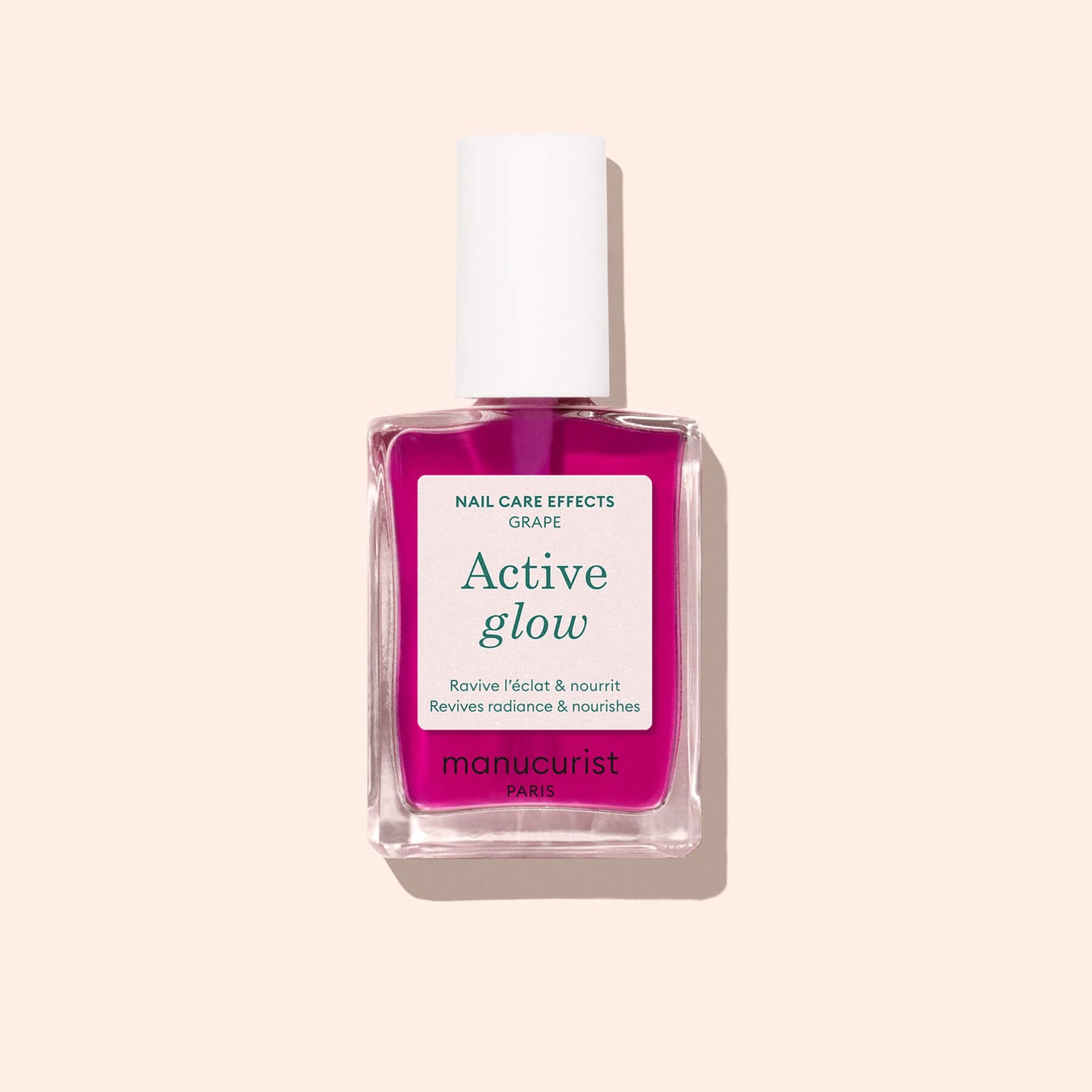 A bottle of Manucurist Active Glow Grape nail care polish with a white cap and pink liquid is shown against a light beige background. The label highlights that it revives radiance, nourishes nails, and enhances natural shine.