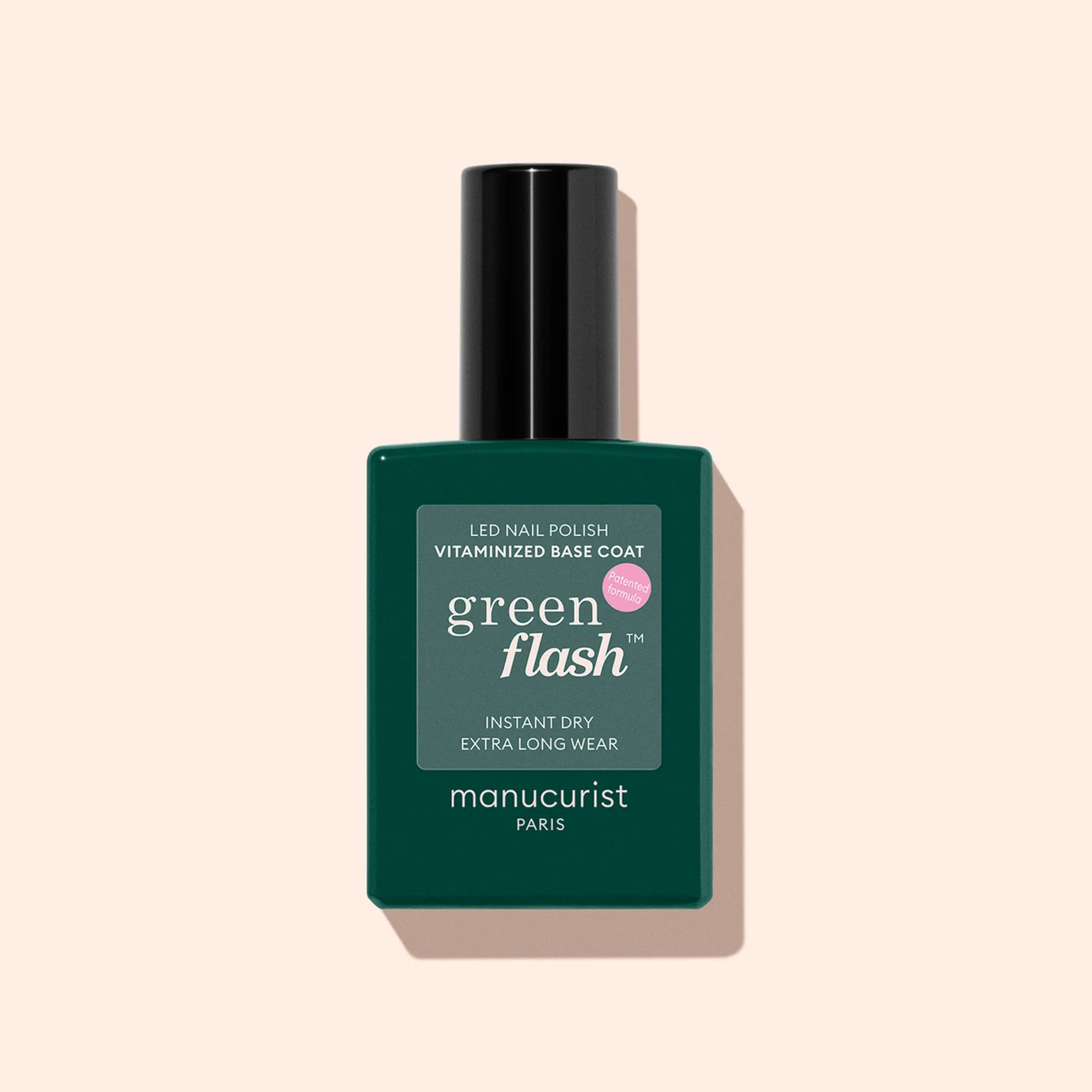 A bottle of Manucurist Vitaminised Base Coat Green Flash™ with a black cap sits on a light beige background. The green label displays white and light pink text and promotes its nail-fortifying KeraHCE+ technology.