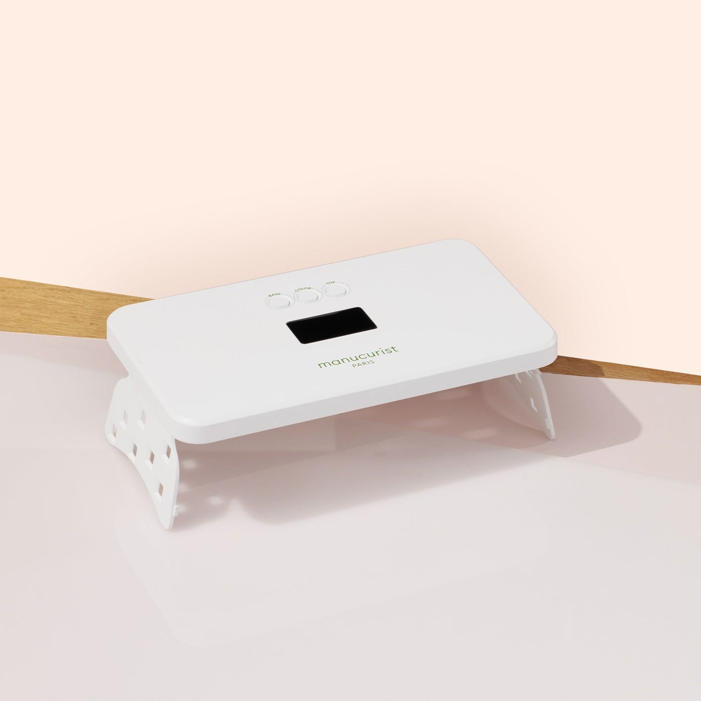 The Manucurist Premium Lamp is a white, rectangular LED lamp with a digital display, shown on a light pink and beige surface—ideal for flawless gel polish manicures or curing Green Flash nails.