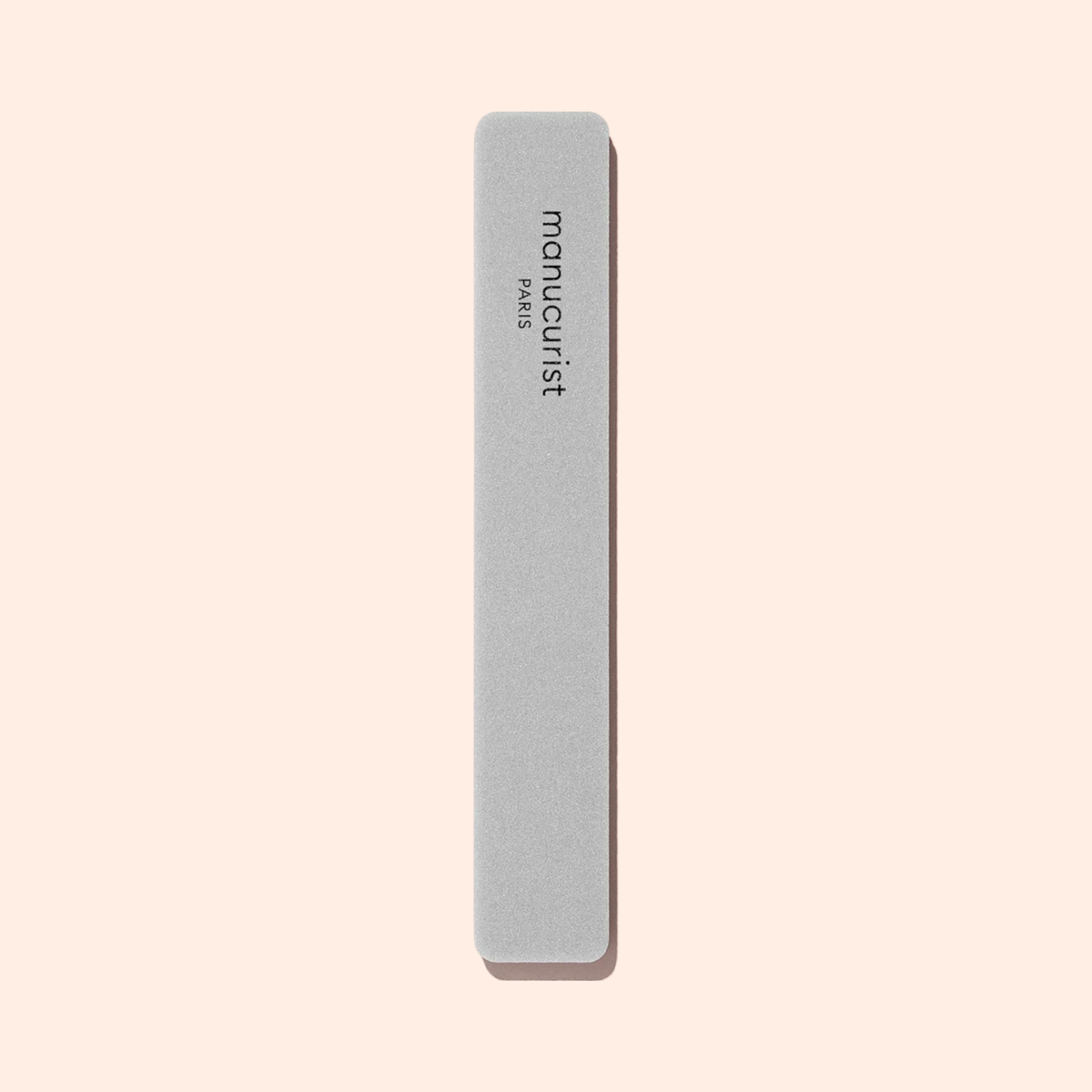 A light gray Nail buffer sponge by Manucurist, rectangular with rounded edges and “manucurist PARIS” printed vertically, is shown on a plain beige background.