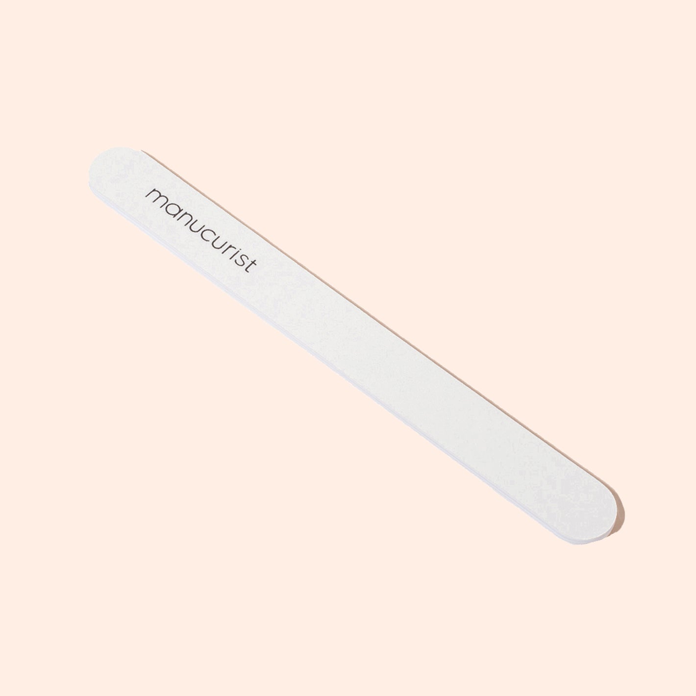 A Manucurist 100/180 emery board for natural nails with rounded edges and the brand name printed on it, featuring soft and coarse grits, displayed on a pale peach background.