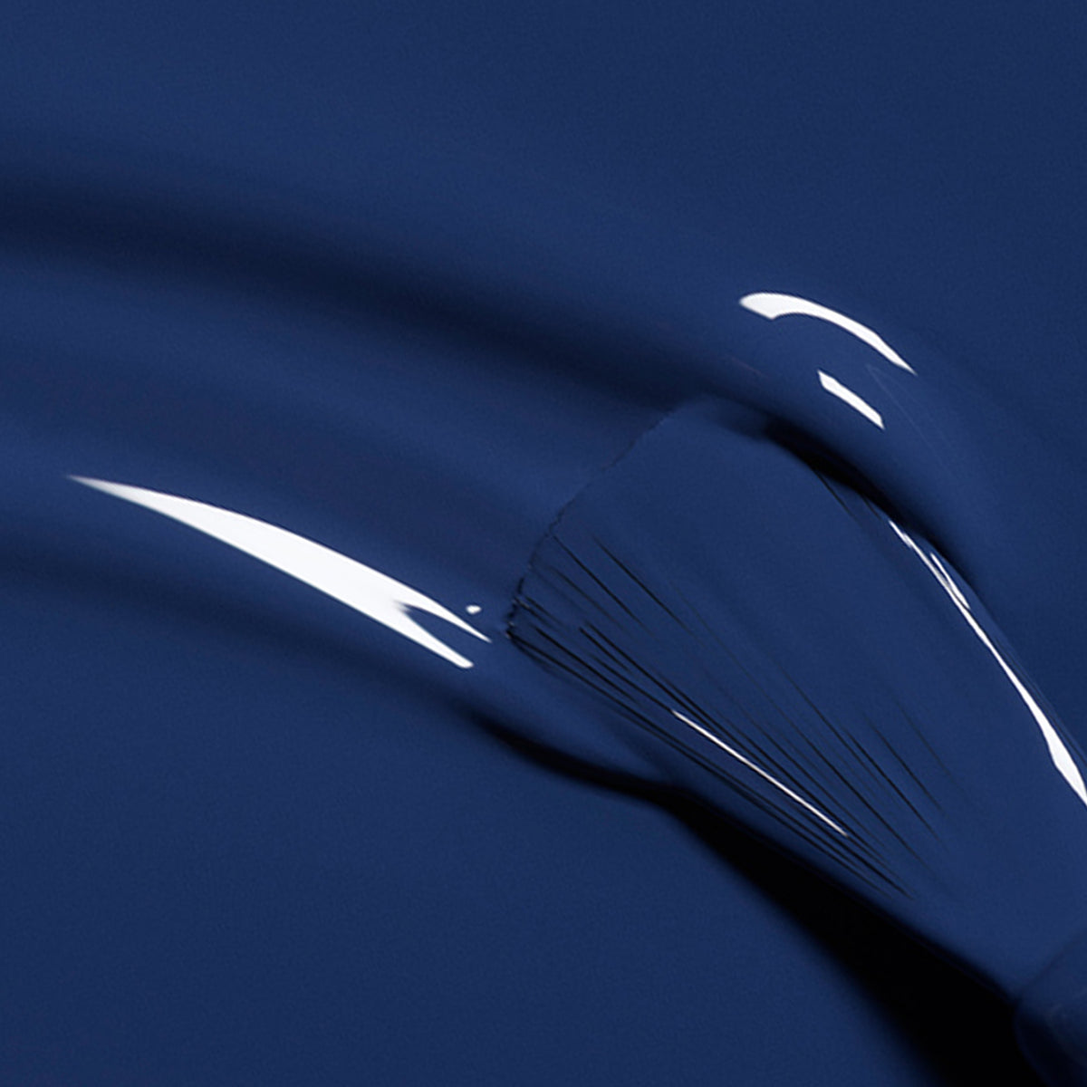 A close-up of a brush gliding through Manucurist’s Midnight, a glossy dark blue polish, creating smooth, reflective strokes on the nail surface.
