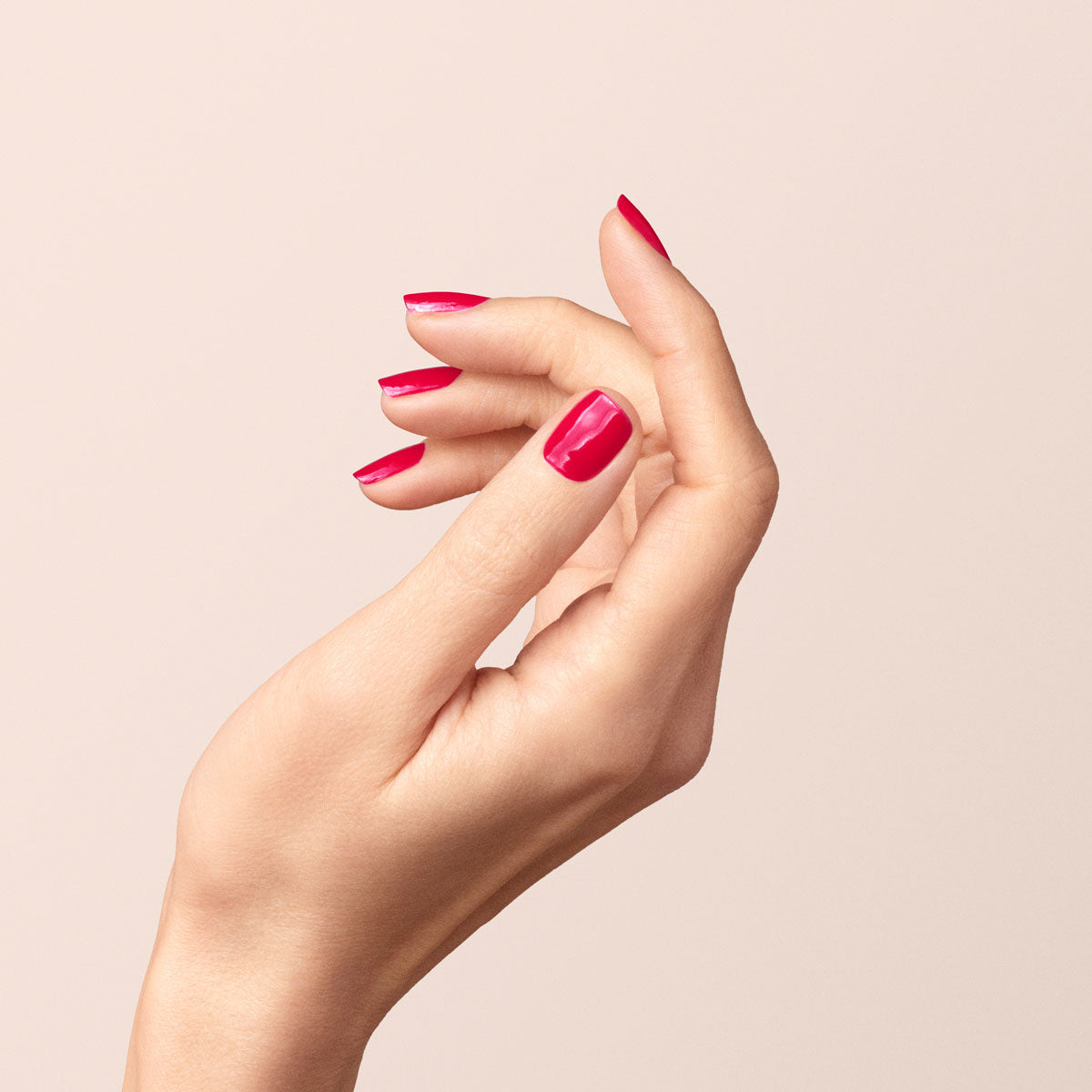 A close-up of a hand with fingers gently curved, featuring neatly manicured nails painted in glossy, bright red Peonie OLD bio-sourced nail polish by Manucurist-test against a plain, light background.
