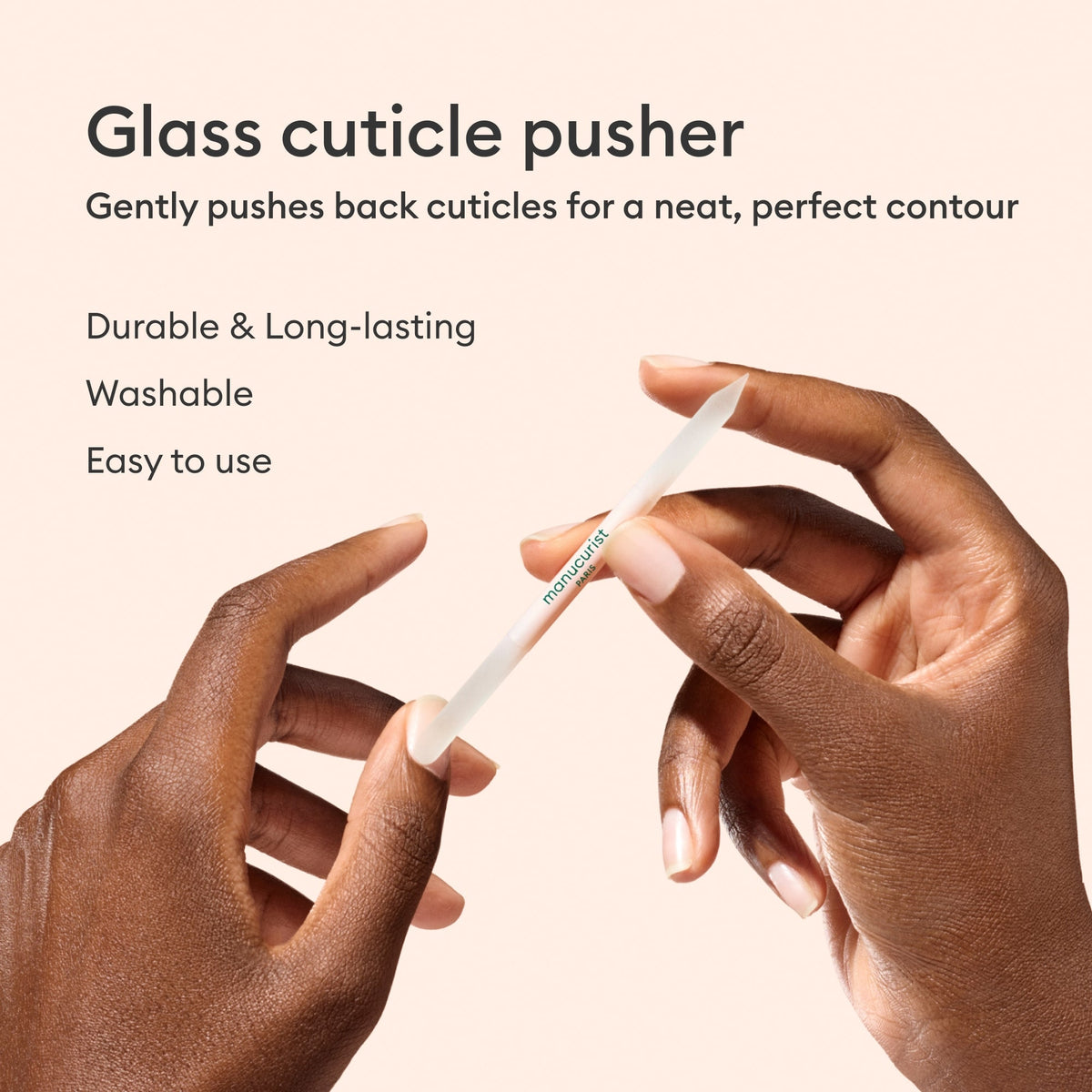 Two hands hold the Manucurist Glass Cuticle Pusher. Text notes its durability, washability, and easy use as it shapes nail contours for a clean finish. Background is light beige.