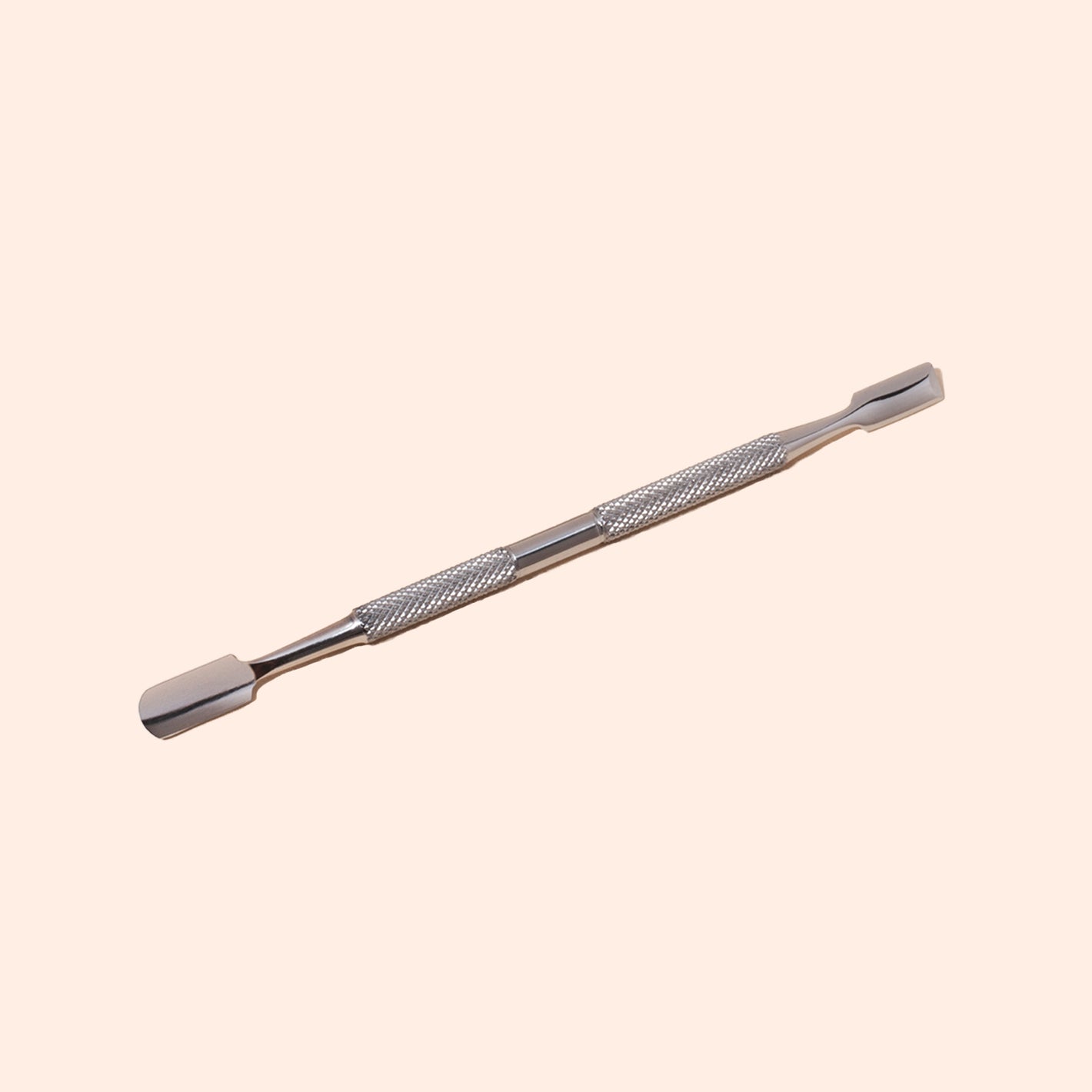 The Manucurist Steel cuticle pusher, featuring a double-ended stainless steel design and textured grip, rests on a light beige background. Both flat, slightly curved tips allow for precise nail care.