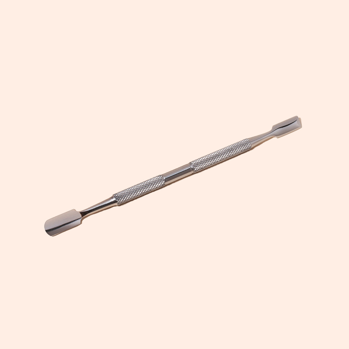 The Manucurist Steel cuticle pusher, featuring a double-ended stainless steel design and textured grip, rests on a light beige background. Both flat, slightly curved tips allow for precise nail care.