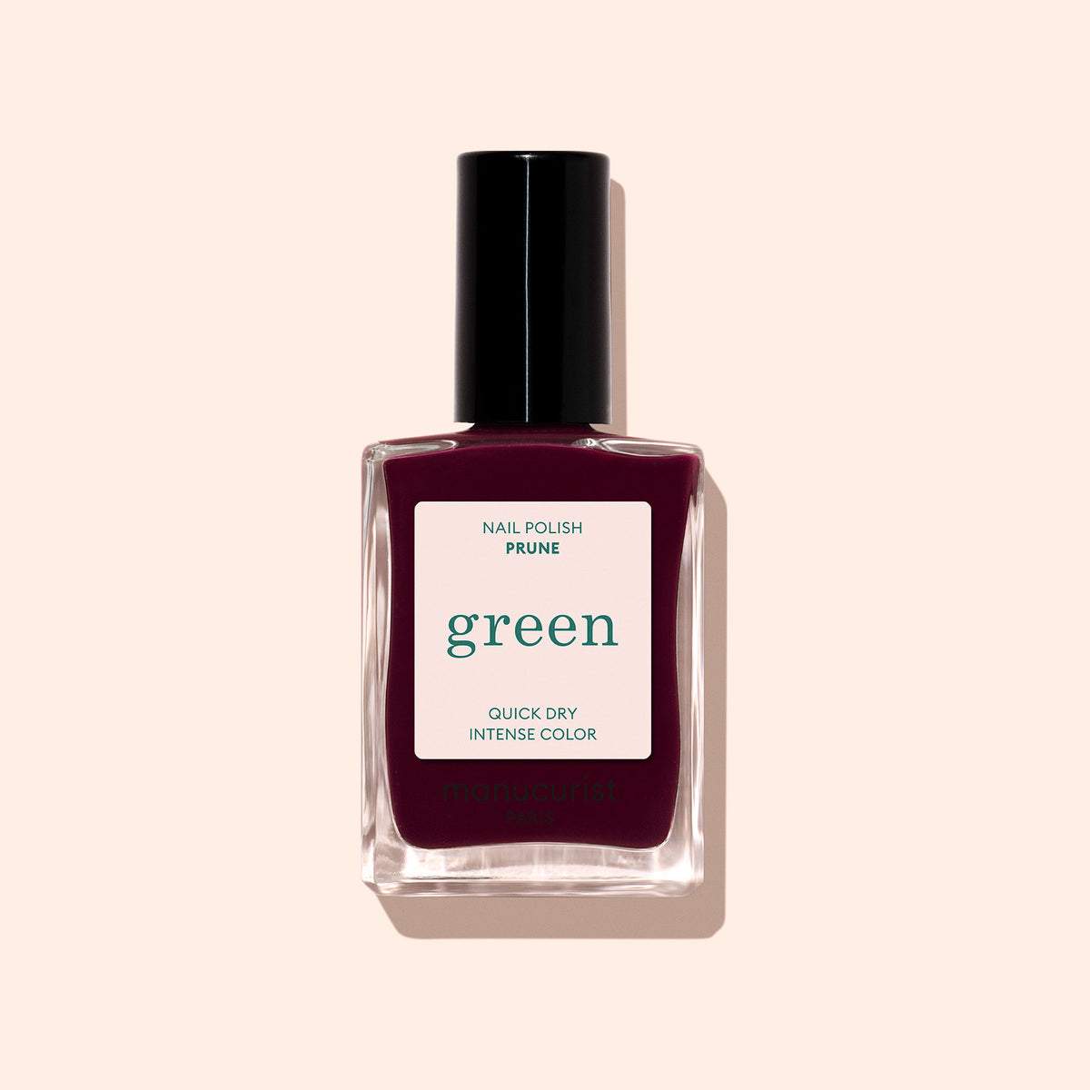 A bottle of Manucurist nail polish in the shade Prune, a dark burgundy color with a black cap, is displayed against a light beige background.
