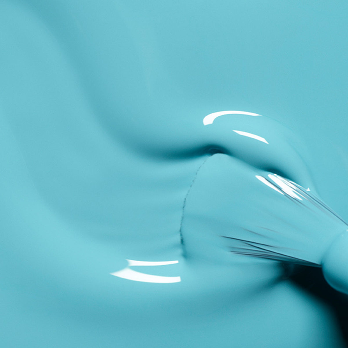 A close-up of a Manucurist nail art brush spreading smooth, glossy Underwater Glitter polish. The bristles and shimmering turquoise paint create gentle waves, perfect for intricate nail art designs.
