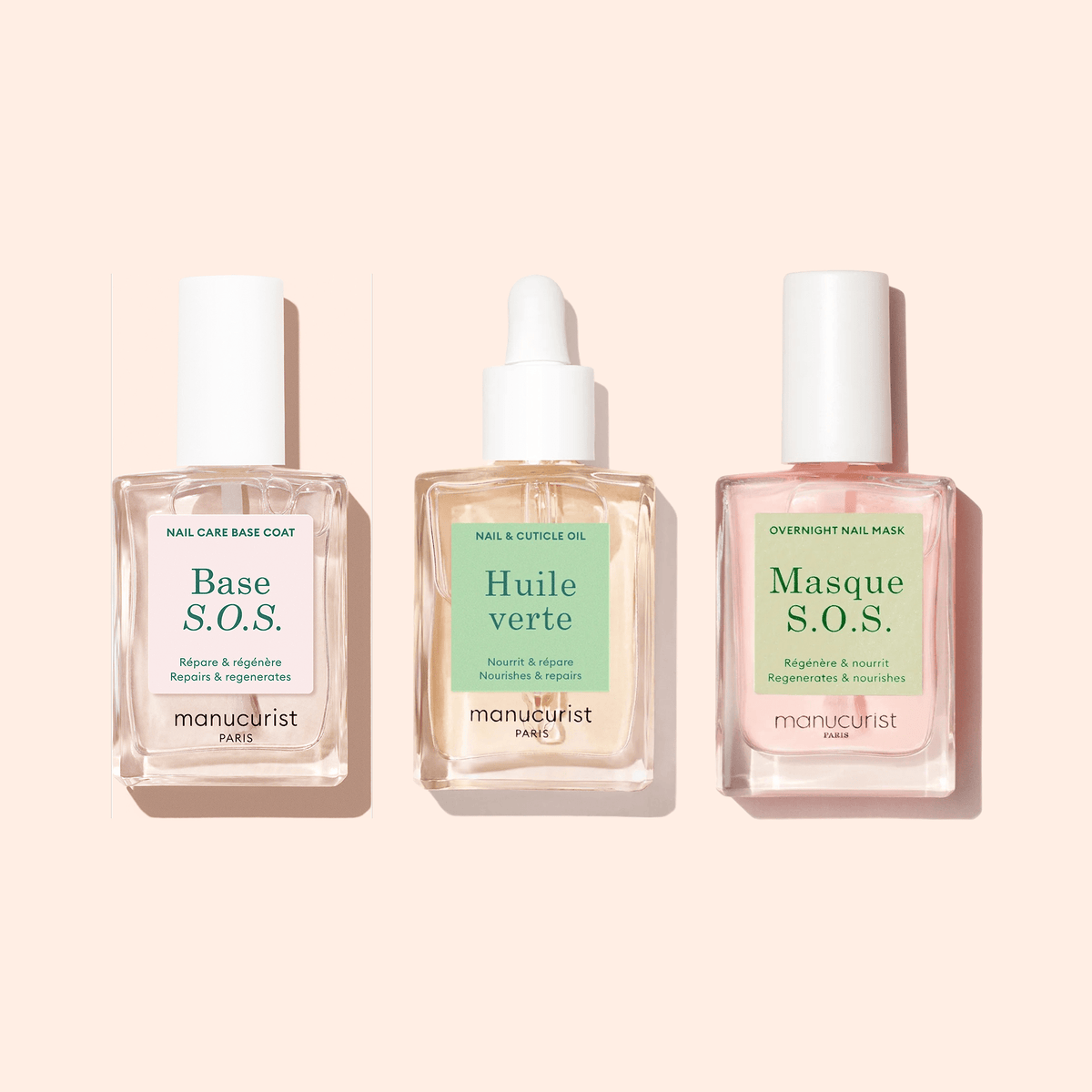 Three clear square bottles of Manucurist S.O.S Nail Strengthener sit in a row on a pale peach background, labeled Base S.O.S., Huile verte, and Masque S.O.S.—each formulated for nail repair and strengthening.
