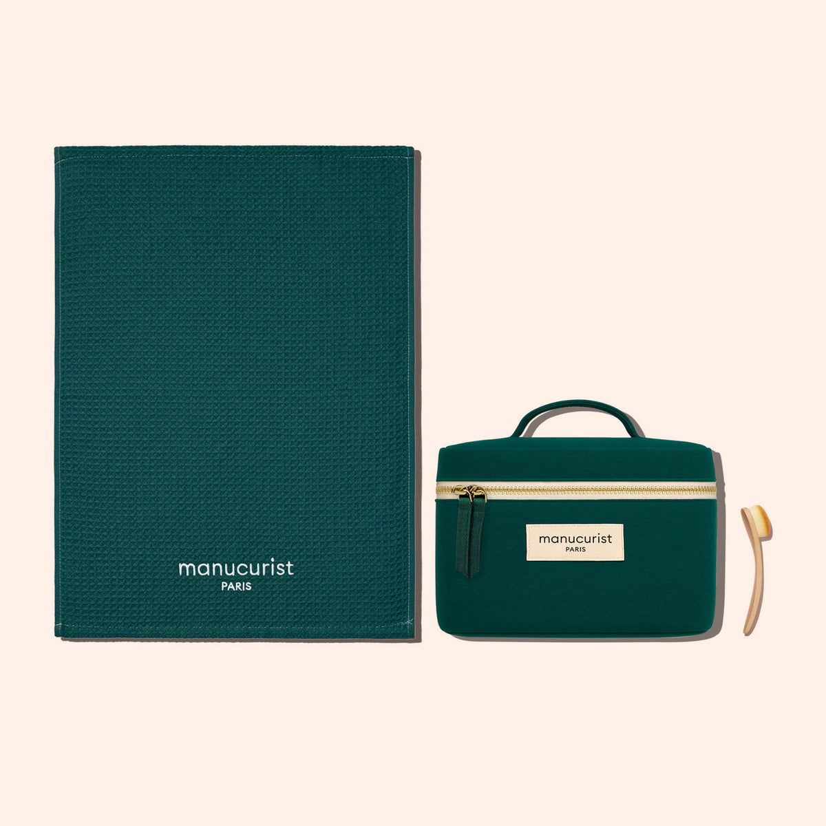 A dark green Manucurist Towel made from organic cotton, paired with a matching Manucurist zippered pouch with handle and label, and a small wooden manicure tool, all set against a light beige background.