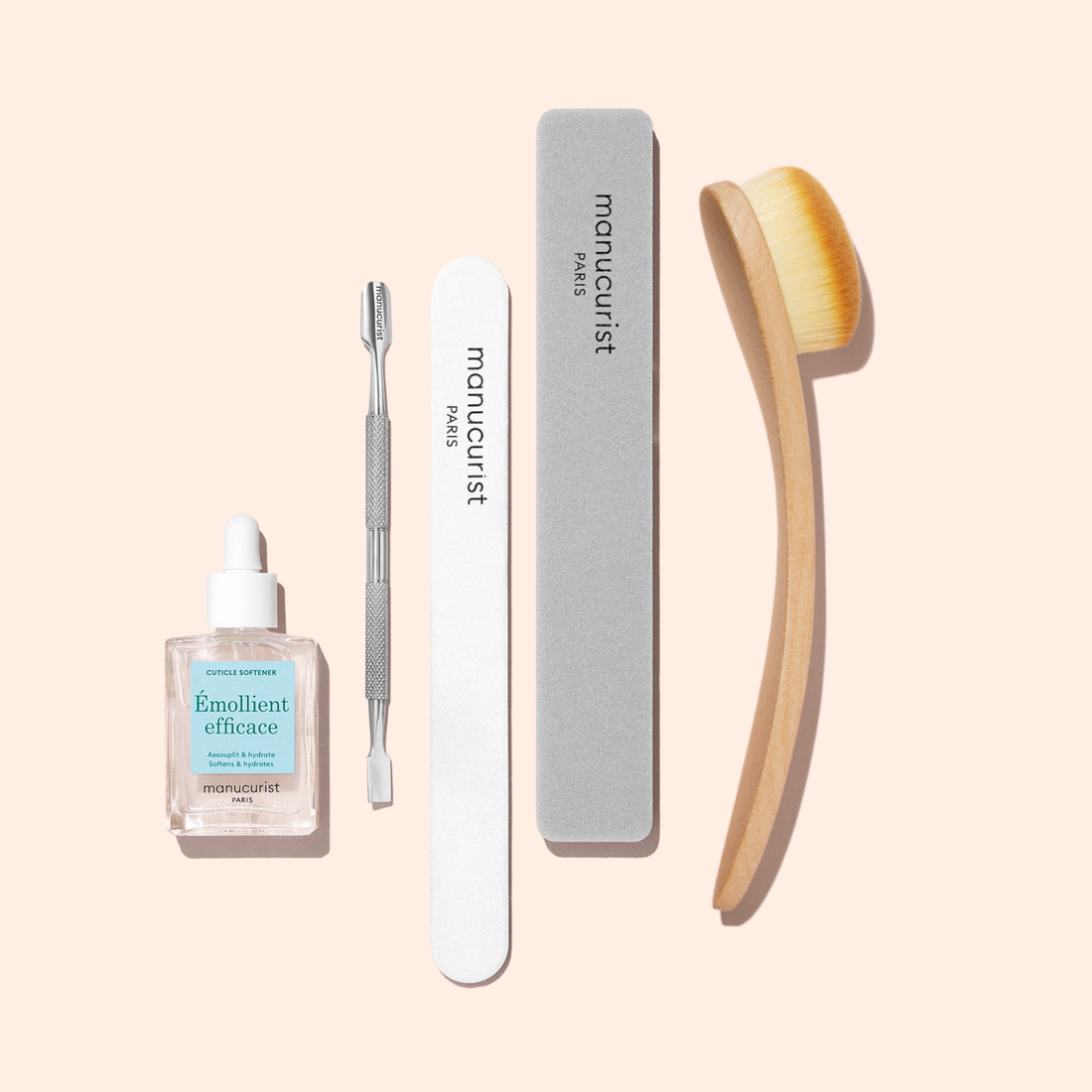 A set of nail care tools on a light background, featuring a bottle of cuticle softener, metal cuticle pusher, nail file, gray buffer block, and the Manucurist Dust Brush with vegan bristles for gently cleaning the nail surface.
