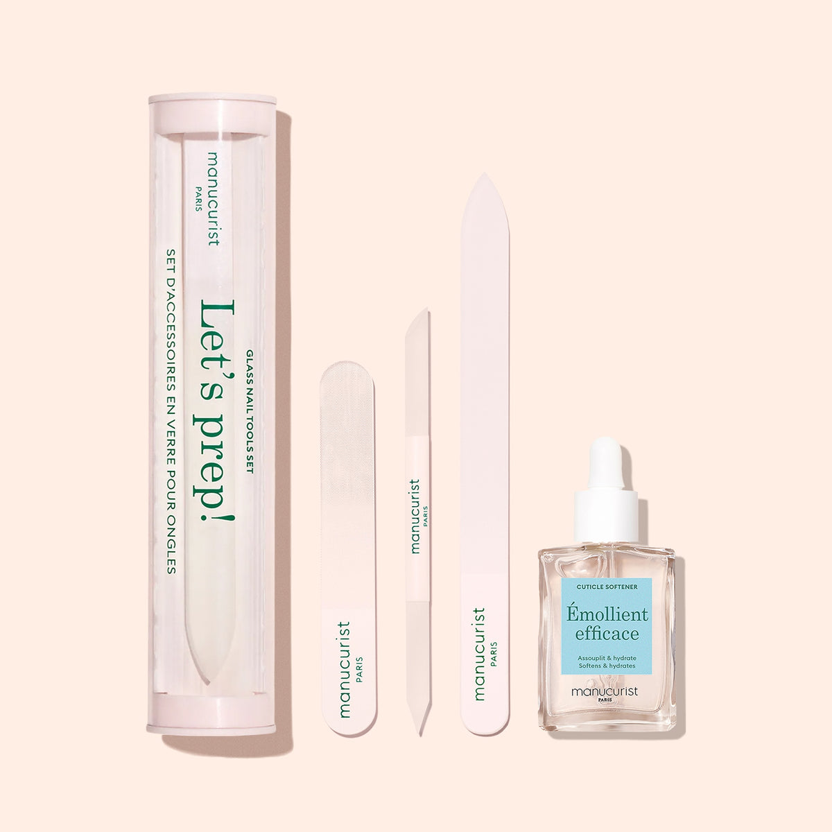 The Manucurist Nail Prep Set—featuring a cylindrical case, glass nail file, two emery boards, and Émollient efficace cuticle remover—is arranged on a pale pink background.