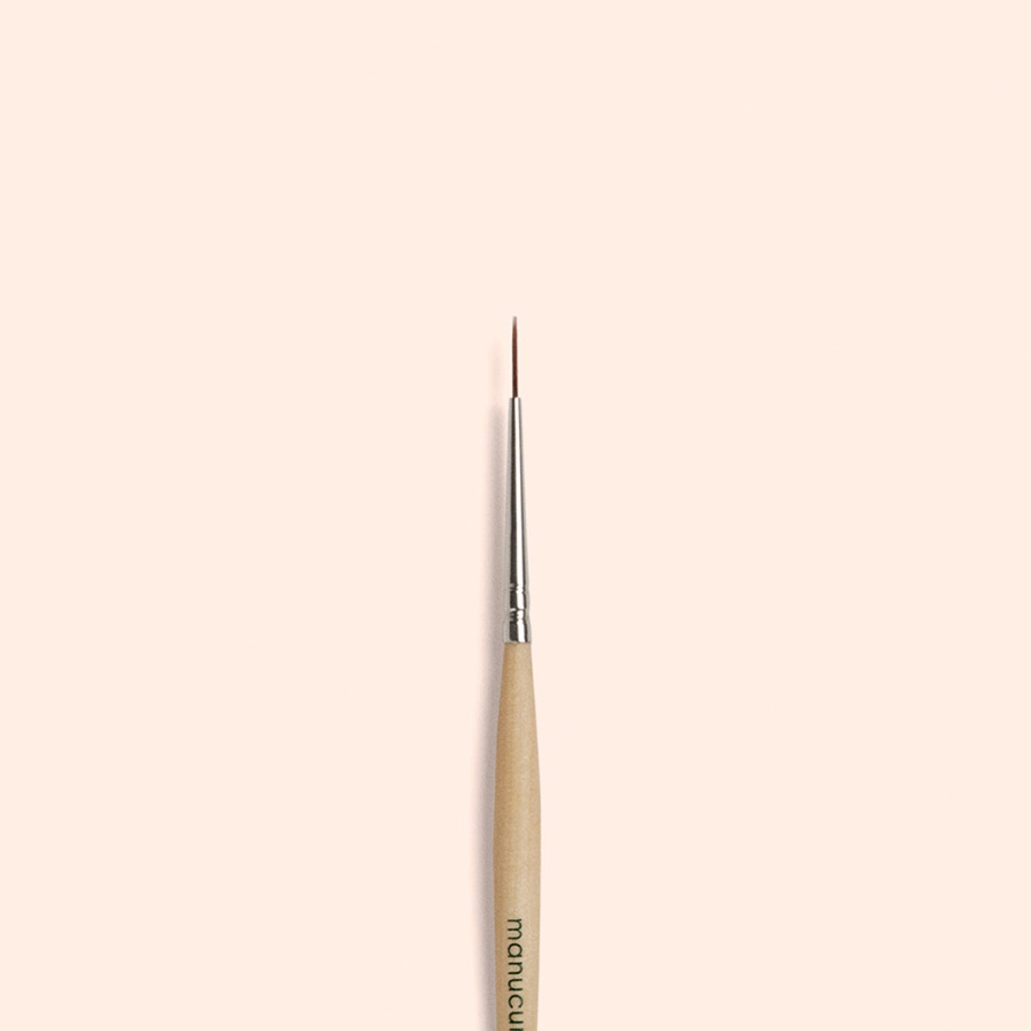 The Manucurist Liner Brush, featuring a thin, fine tip with a wooden handle and silver ferrule, is centered vertically on a plain beige background—perfect for creating precise nail art designs.