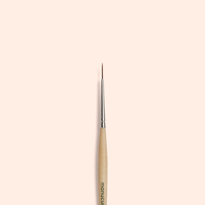 The Manucurist Liner Brush, featuring a thin, fine tip with a wooden handle and silver ferrule, is centered vertically on a plain beige background—perfect for creating precise nail art designs.