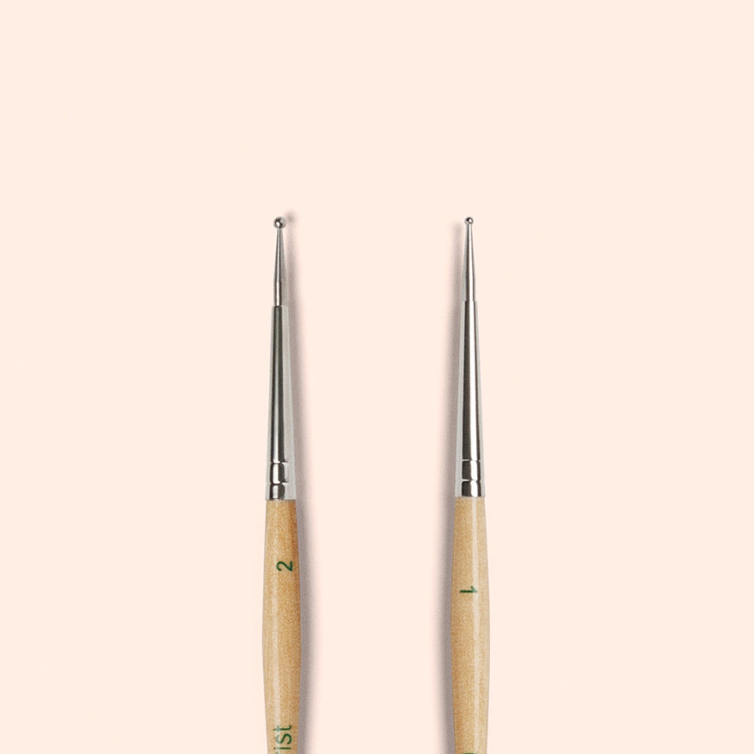 Two Manucurist Dotting Tools with metal tips and wooden handles stand upright side by side on a beige background—ideal for precise nail art designs in your tool collection.