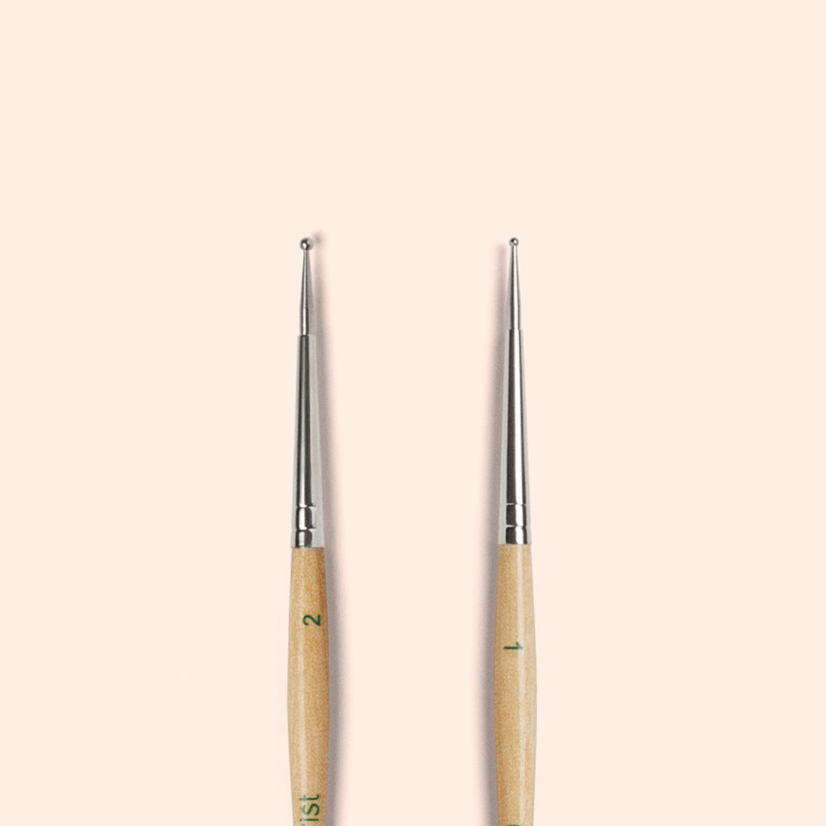 Two Manucurist Dotting Tools with metal tips and wooden handles stand upright side by side on a beige background—ideal for precise nail art designs in your tool collection.