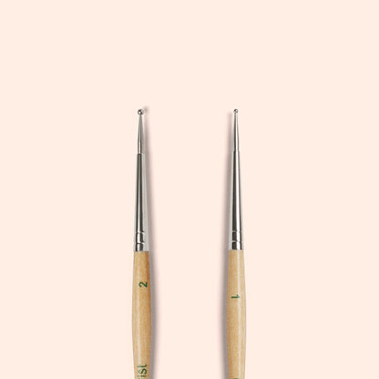 Two Manucurist Dotting Tools with metal tips and wooden handles stand upright side by side on a beige background—ideal for precise nail art designs in your tool collection.