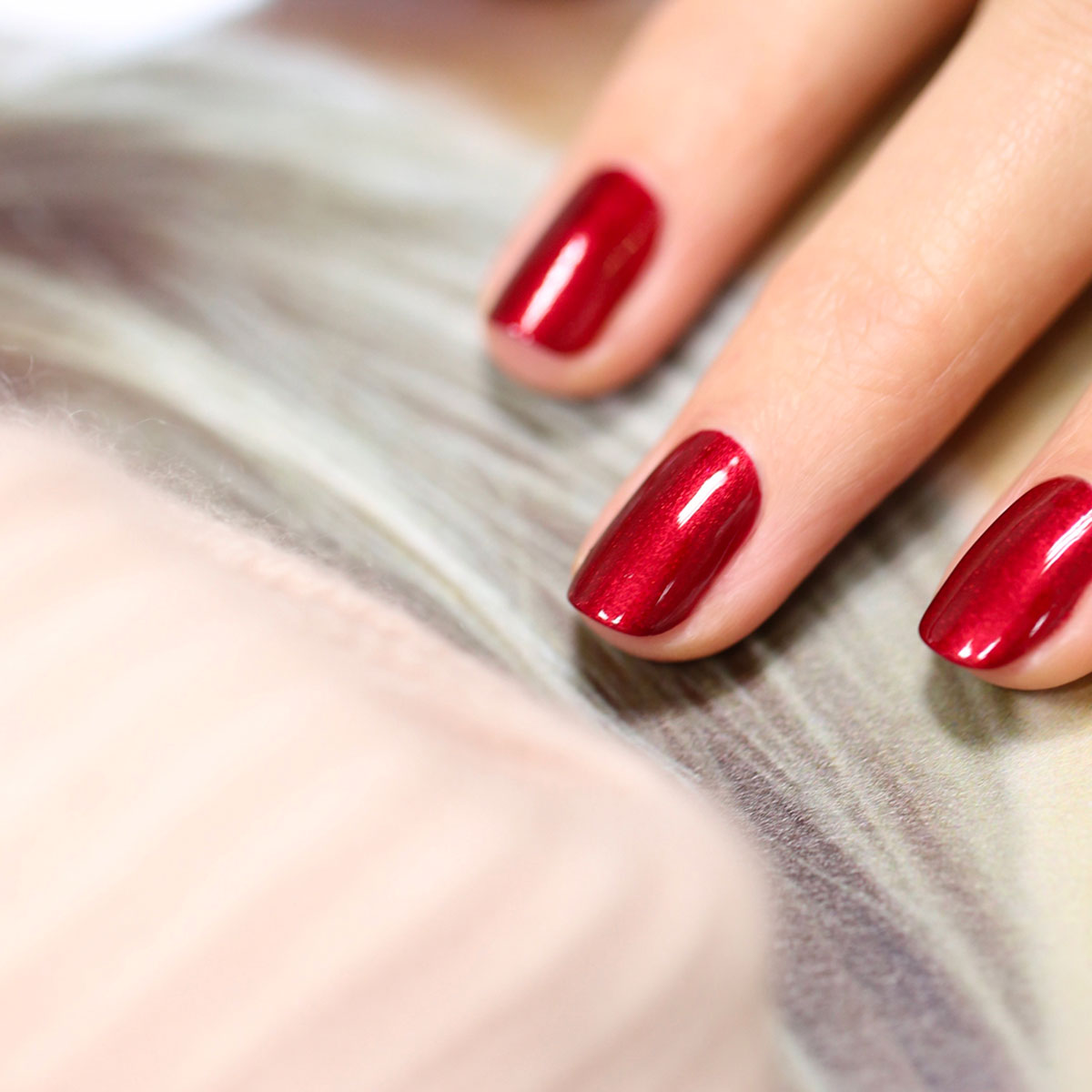 A close-up of a hand with neatly manicured nails painted in Red Hibiscus polish from Manucurist, resting on a soft, blurred background.