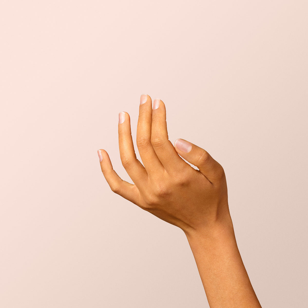 A hand with light brown skin and neatly manicured nails painted in Manucurist’s Diamant, a sleek silver shade, is raised against a plain, light beige background. The relaxed fingers are slightly spread apart.