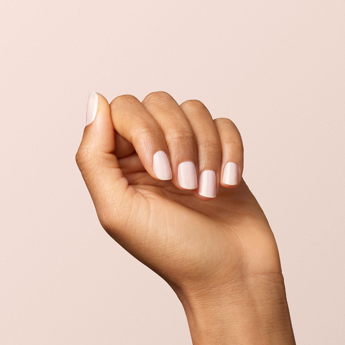 A hand with neatly manicured nails painted in Manucurist-test’s Milky white OLD gel nail polish is held up against a plain, light beige background.