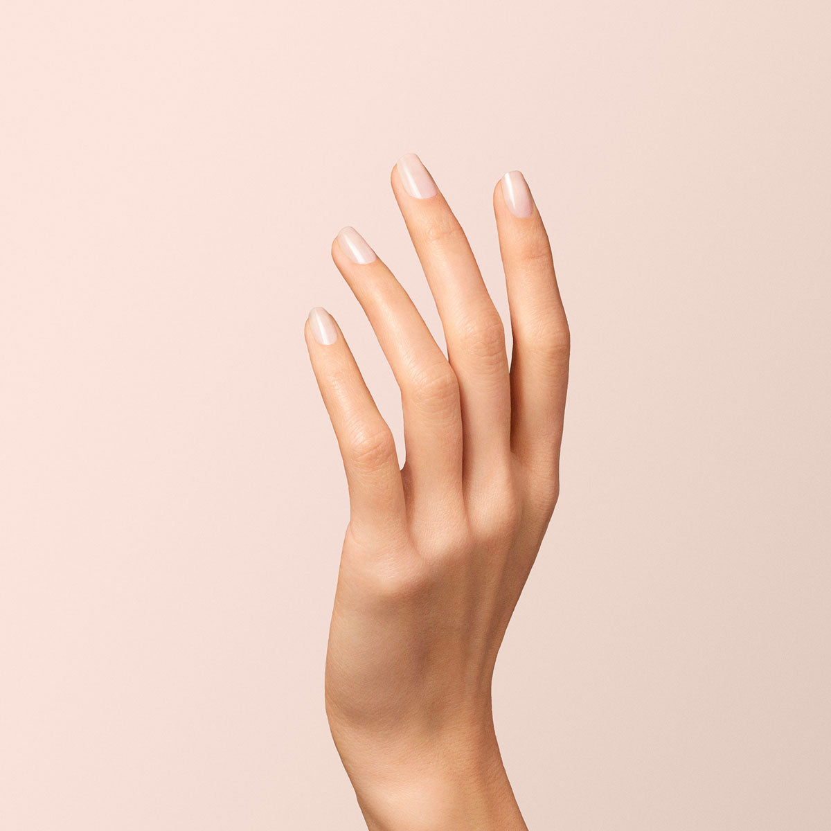 A close-up of a raised hand with fingers slightly bent, showcasing neatly manicured nails painted in Manucurist-test’s Milky white OLD gel nail polish, set against a plain beige background.