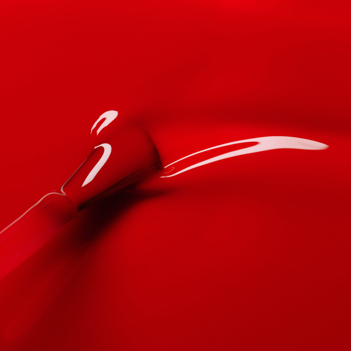 A close-up of the Manucurist Anémone brush creating a smooth stroke in glossy, vivid red gel polish, with reflections highlighting its shiny finish.