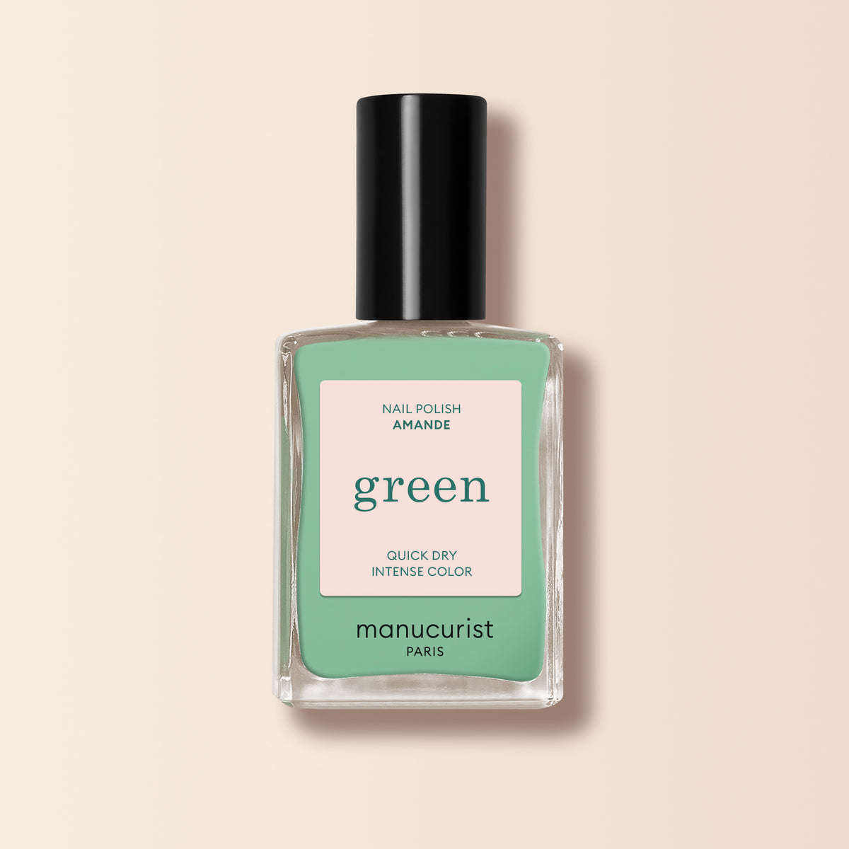 A clear glass bottle of Manucurist Amande nail polish, almond green shade with a black cap. The label reads "Quick dry, intense color, Green™ range." Set against a light beige background.