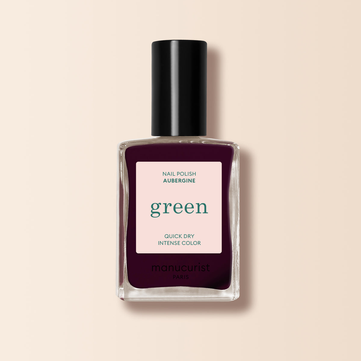 A bottle of Manucurist Aubergine nail polish, quick dry with intense color, sits on a beige background. The rich, deep purple polish is from the Paris Green™ range and is labeled green.