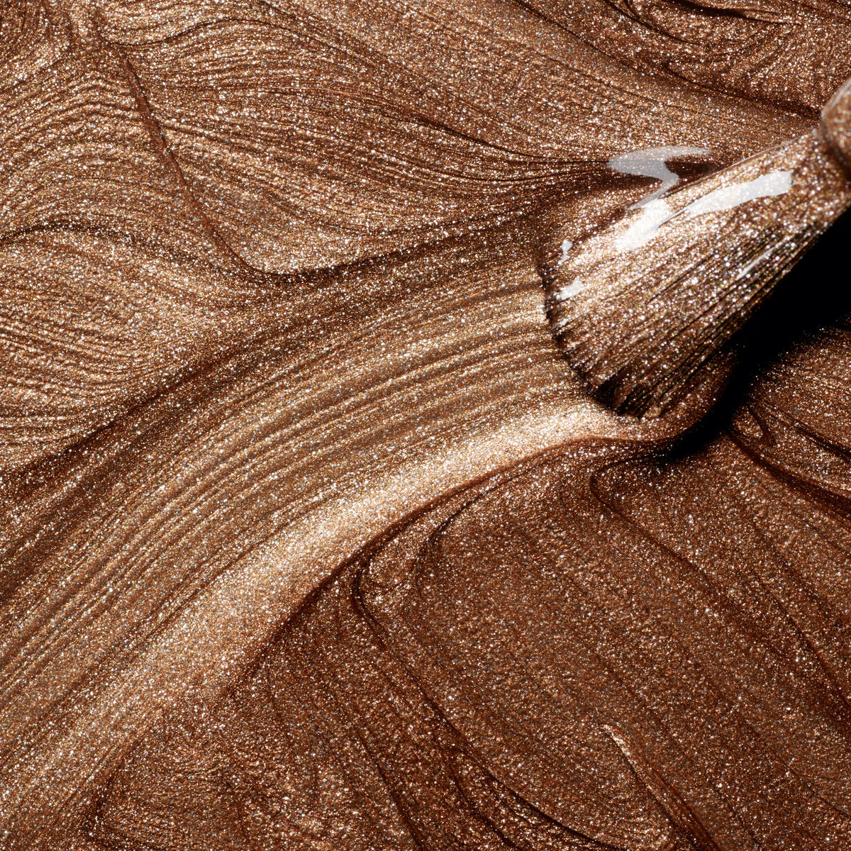 Close-up of a brush applying Manucurist Bronzé, spreading shimmery bronze polish with smooth, metallic swirls and a glossy copper finish.