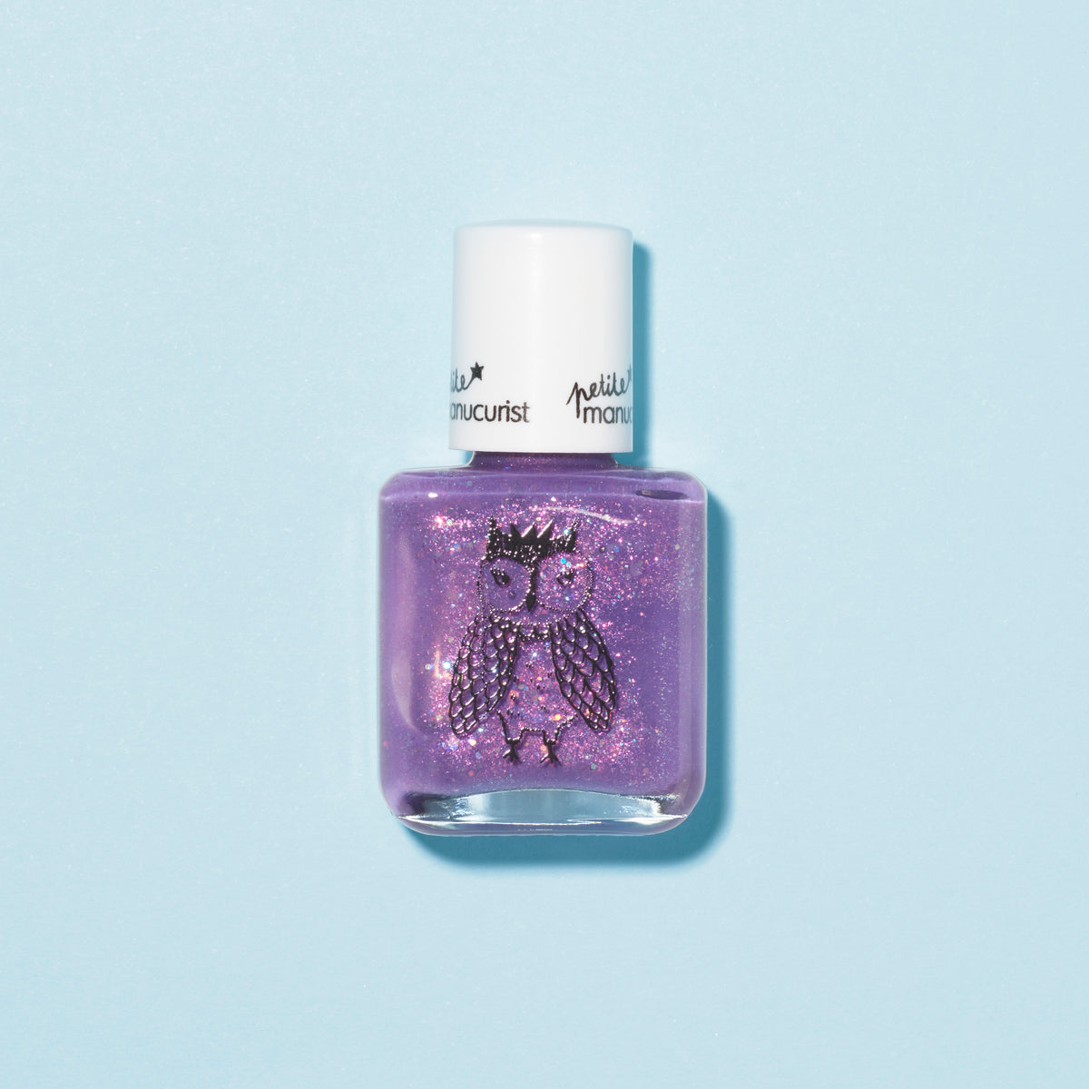 A bottle of Manucurist Scarlett the Owl kids nail polish in purple glitter, with a white cap and a crowned owl illustration on the front, shown against a light blue background.