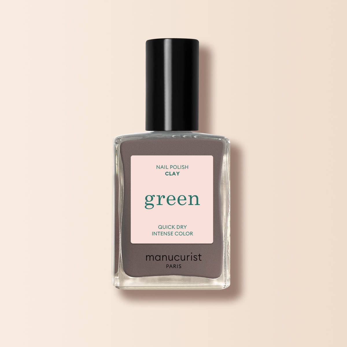 A bottle of Manucurist Clay nail polish, a chestnut gray shade from the Green™ range labeled Quick Dry and Intense Color, with a black cap, is shown against a pale beige background.