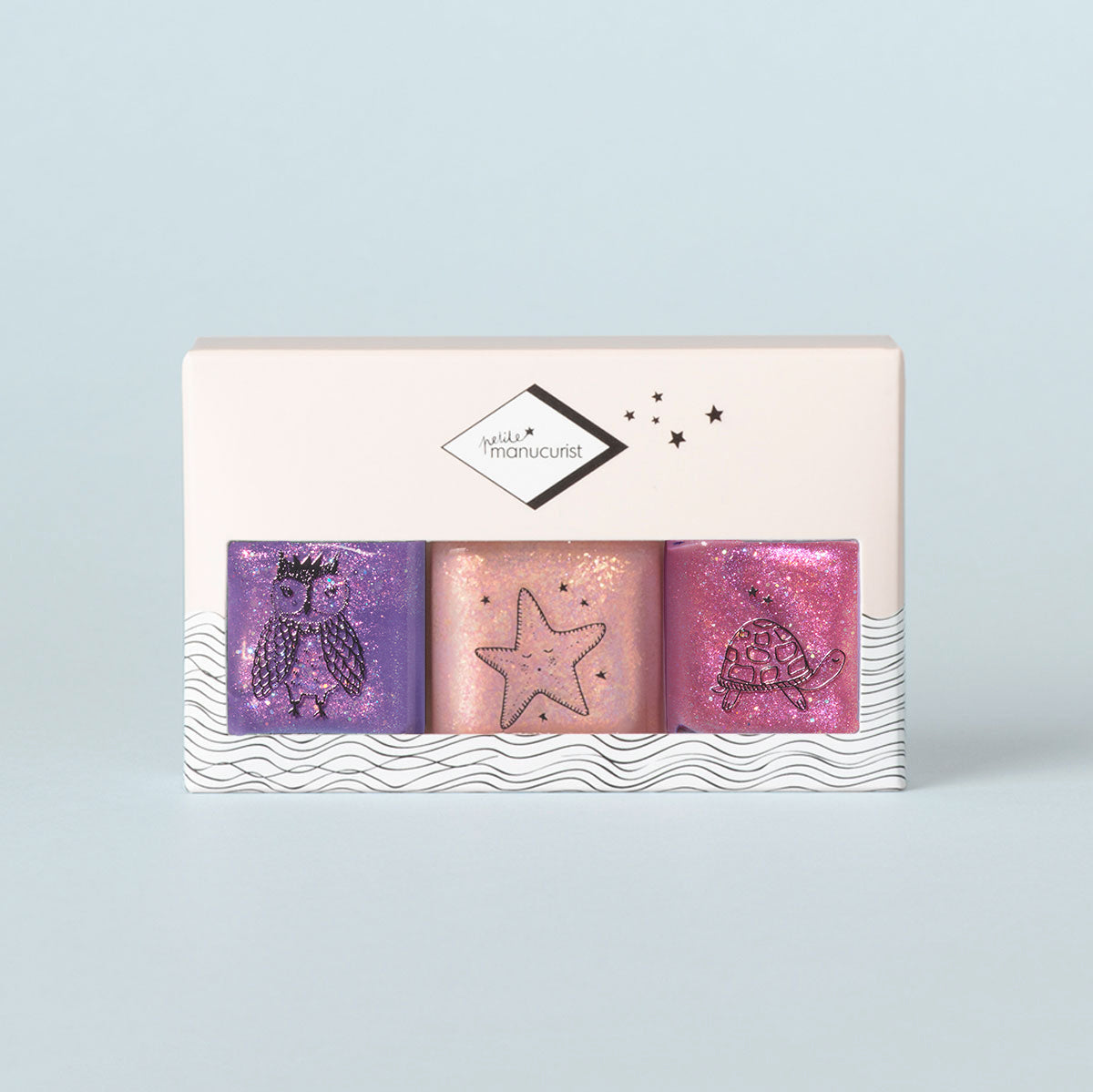 The Manucurist Betty Scarlett Stella set features three glitter nail polishes for kids in purple, peach, and pink, each bottle adorned with a cute owl, starfish, or turtle. Comes in a non-toxic formula and a light box with wave design.