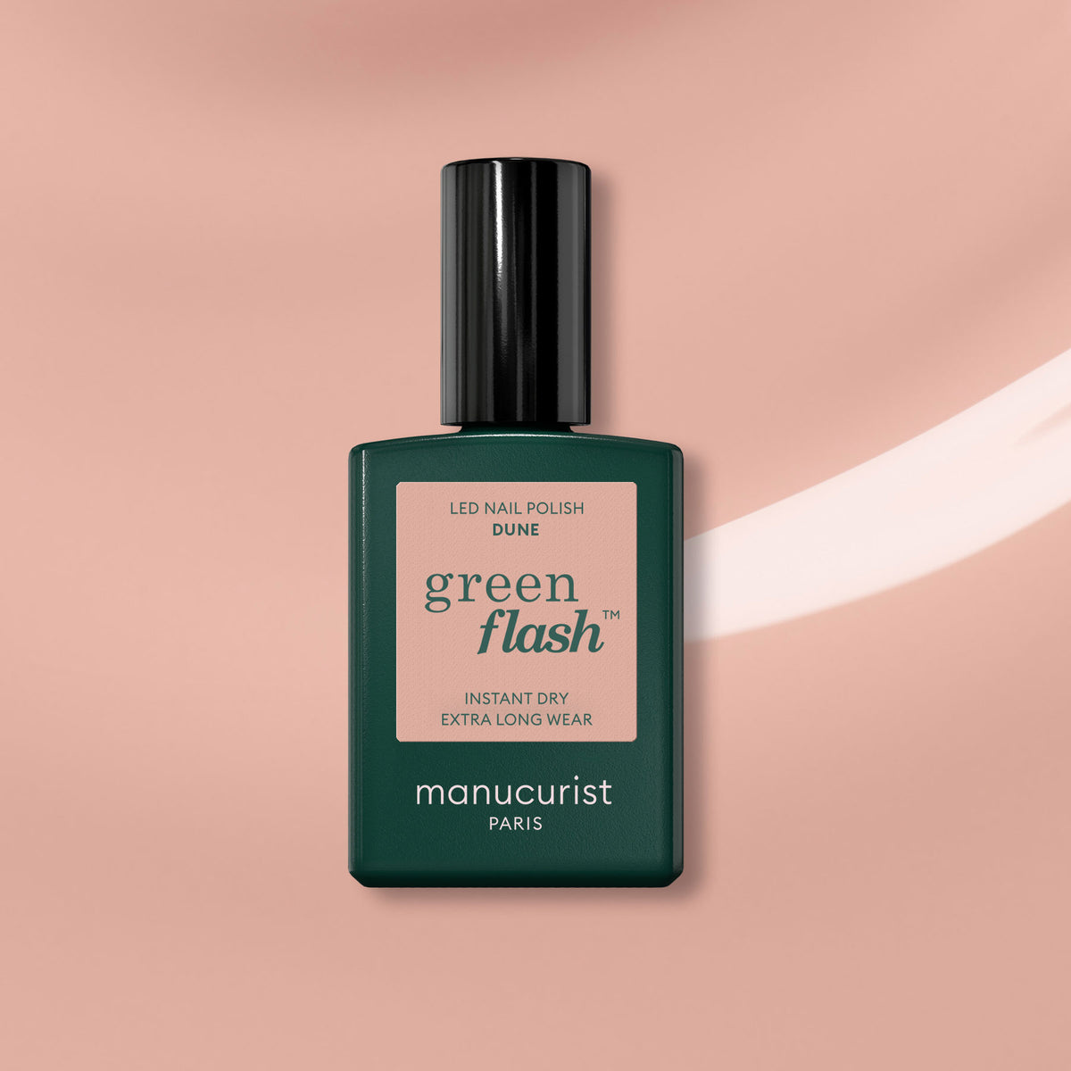 A bottle of Manucurist Dune gel polish is shown with a dark green cap and label on a pink-beige background with a white brushstroke, highlighting the trendy beige shade.