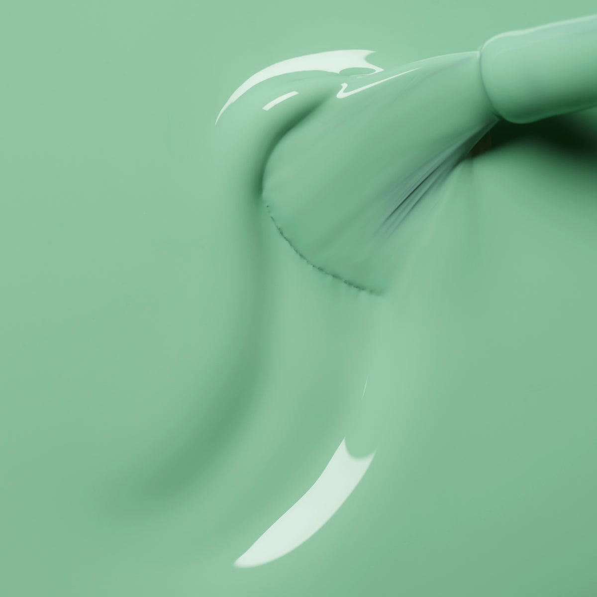 A close-up of a brush applying Amande nail polish from Manucurist in smooth, glossy mint green strokes, showcasing the polish’s texture and the motion of the brush.