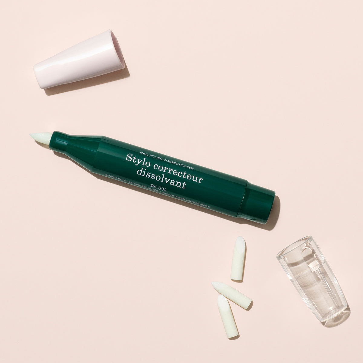The Nail Polish Corrector Pen in dark green, shown with its white cap off, three extra tips, and a clear holder—all set on a pale beige background—ideal for precise gel polish touch-ups.