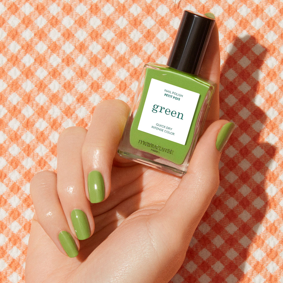 A hand with short, neatly manicured nails painted light green holds a bottle of Manucurist&