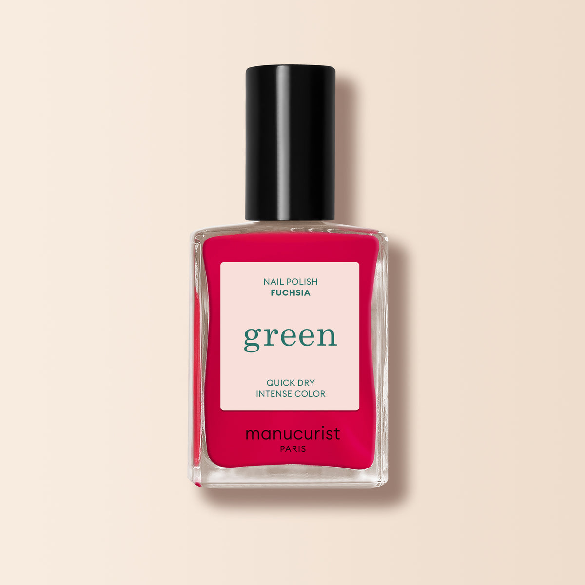 A bottle of Manucurist Fuchsia nail polish features a black cap and a label reading "Nail Polish Fuchsia, green, Quick Dry Intense Color." The bright pinky purple polish pops against a light beige background.